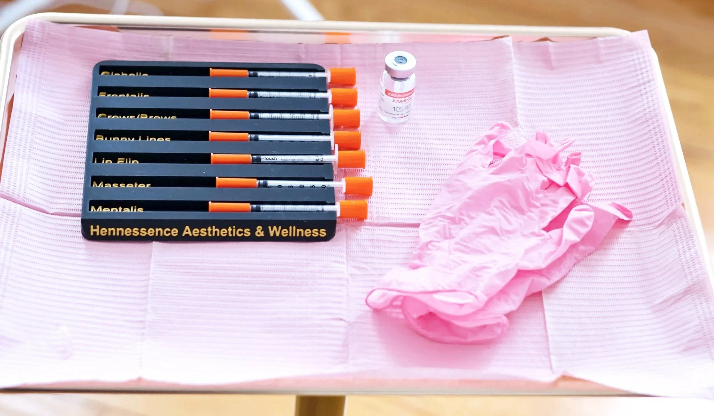 Medical supplies on a pink tray including several syringes, a small vial, pink gloves, and a pair of disposable gloves.