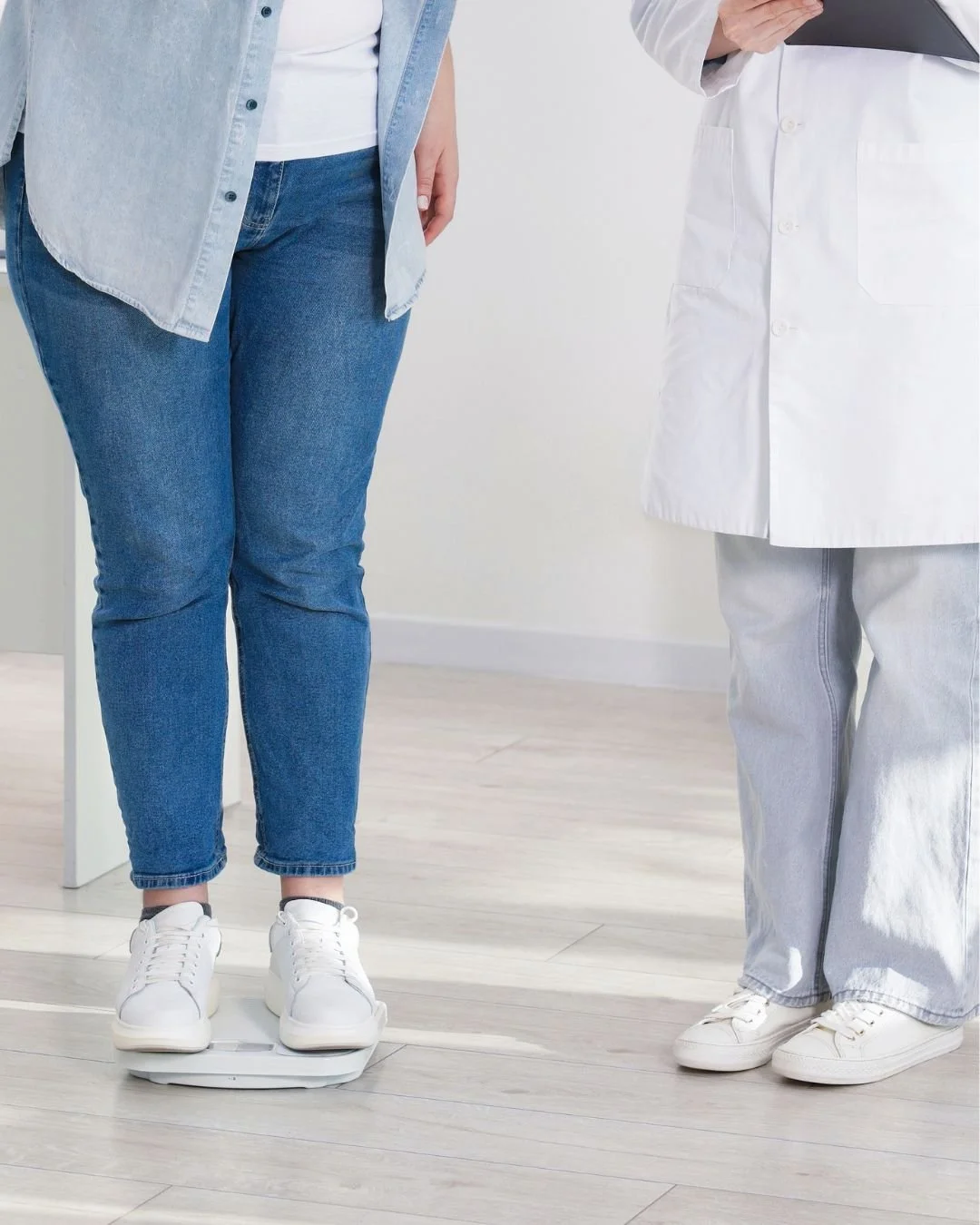 Person standing on a weighing scale while a medical professional in a white coat observes.
