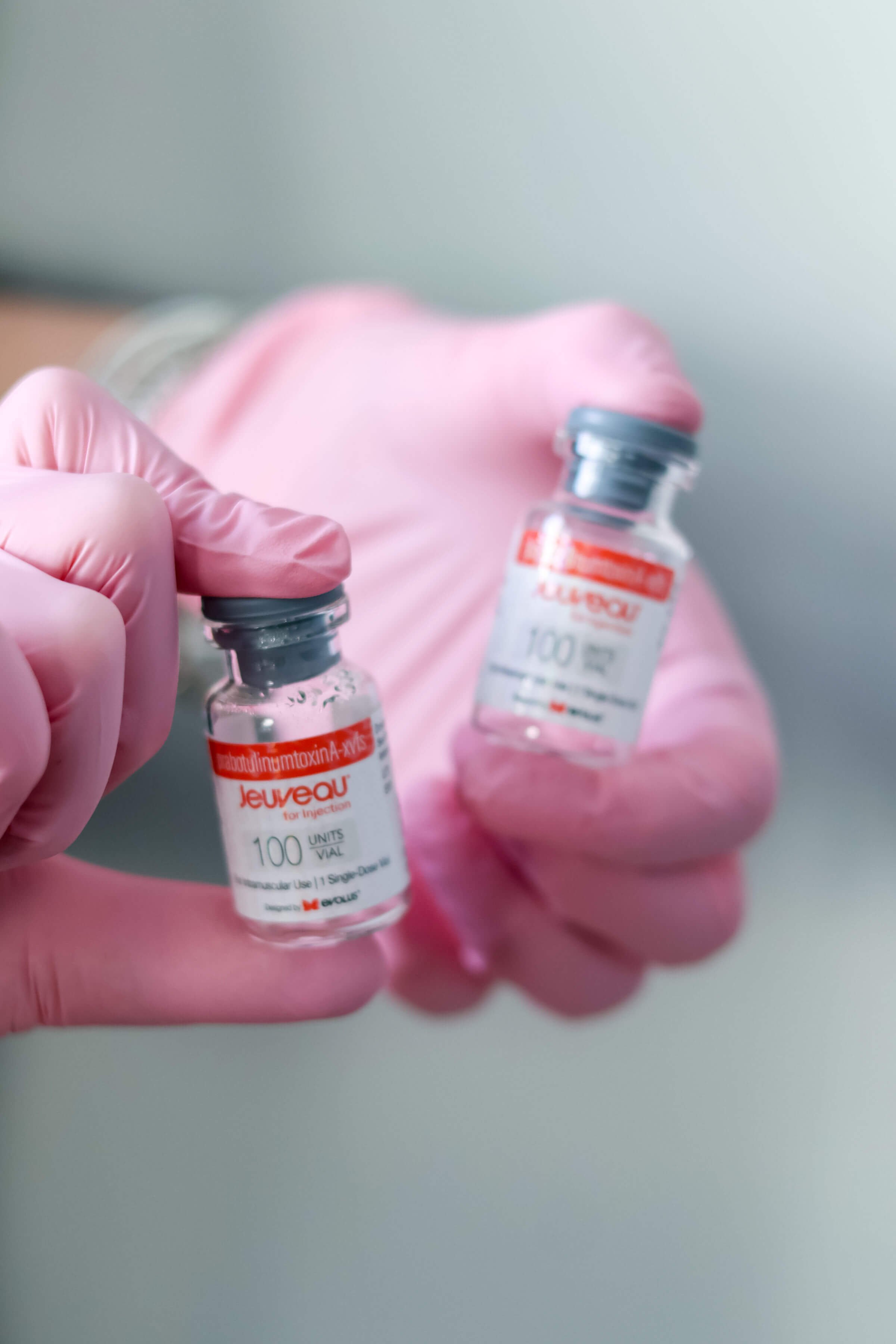A person wearing pink gloves holding two vials of a vaccine.