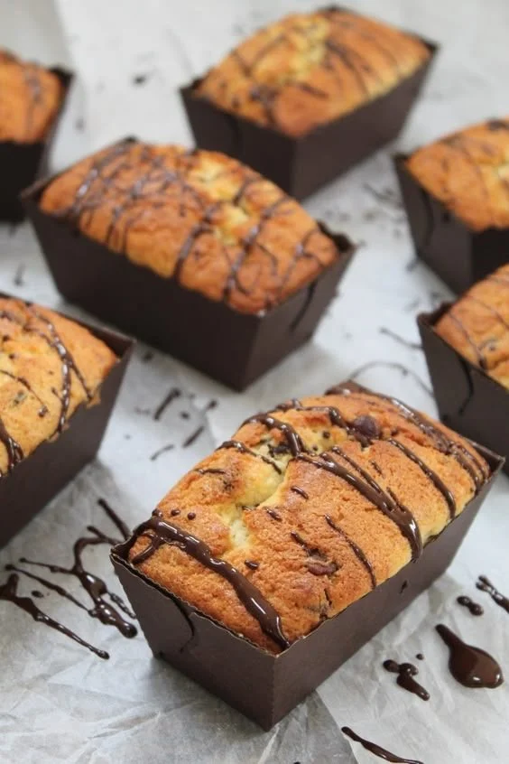 Chocolate-drizzled banana bread loaves in rectangular black pans on parchment paper.