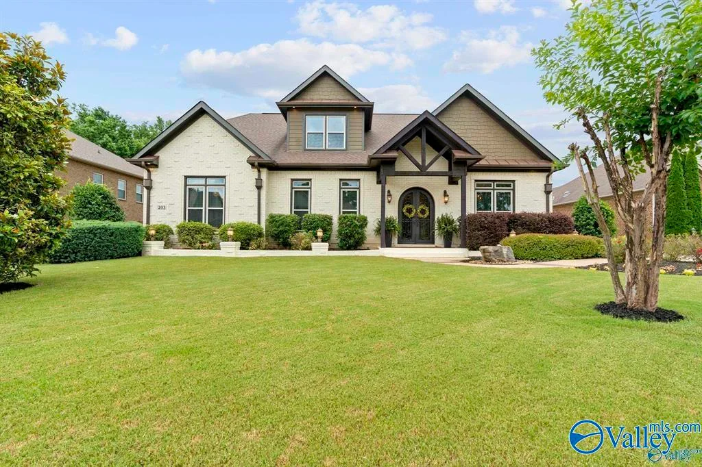 Large, modern house with a well-maintained front lawn, surrounded by trees and bushes, under a partly cloudy sky.