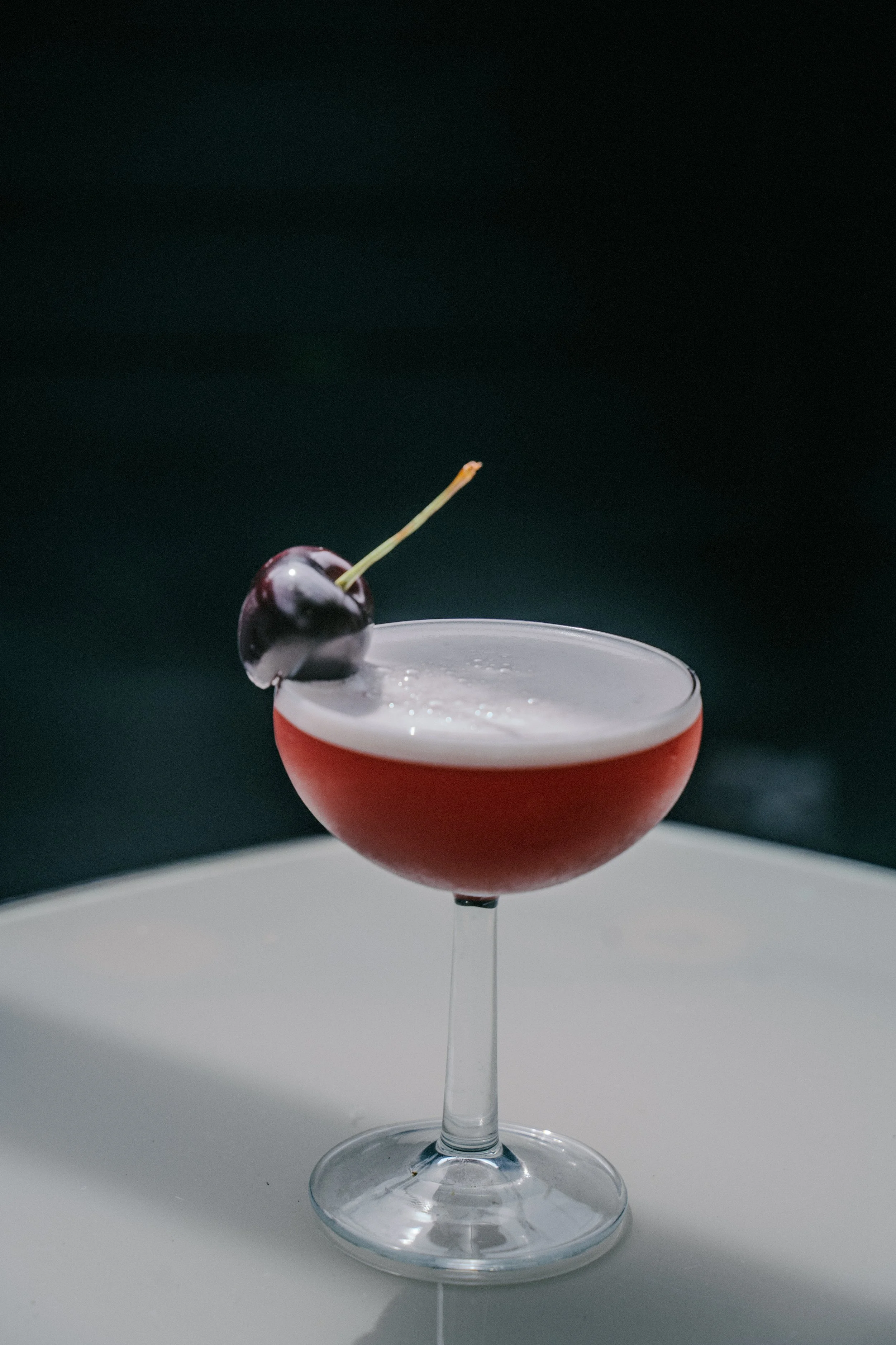 A cocktail in a coupe glass garnished with a cherry.