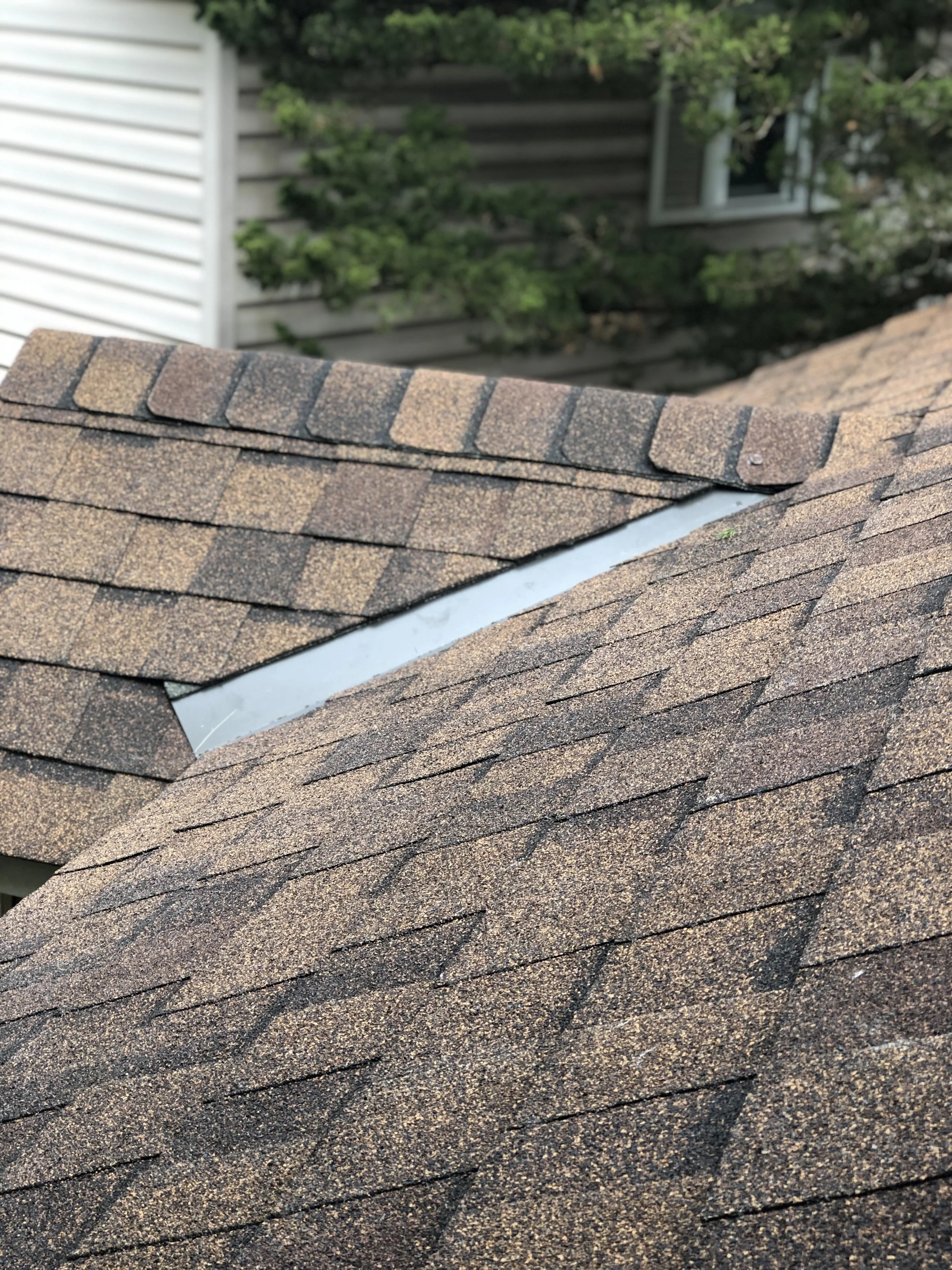 Close-up of a roof with brown asphalt shingles and a metal vent or ridge cap.