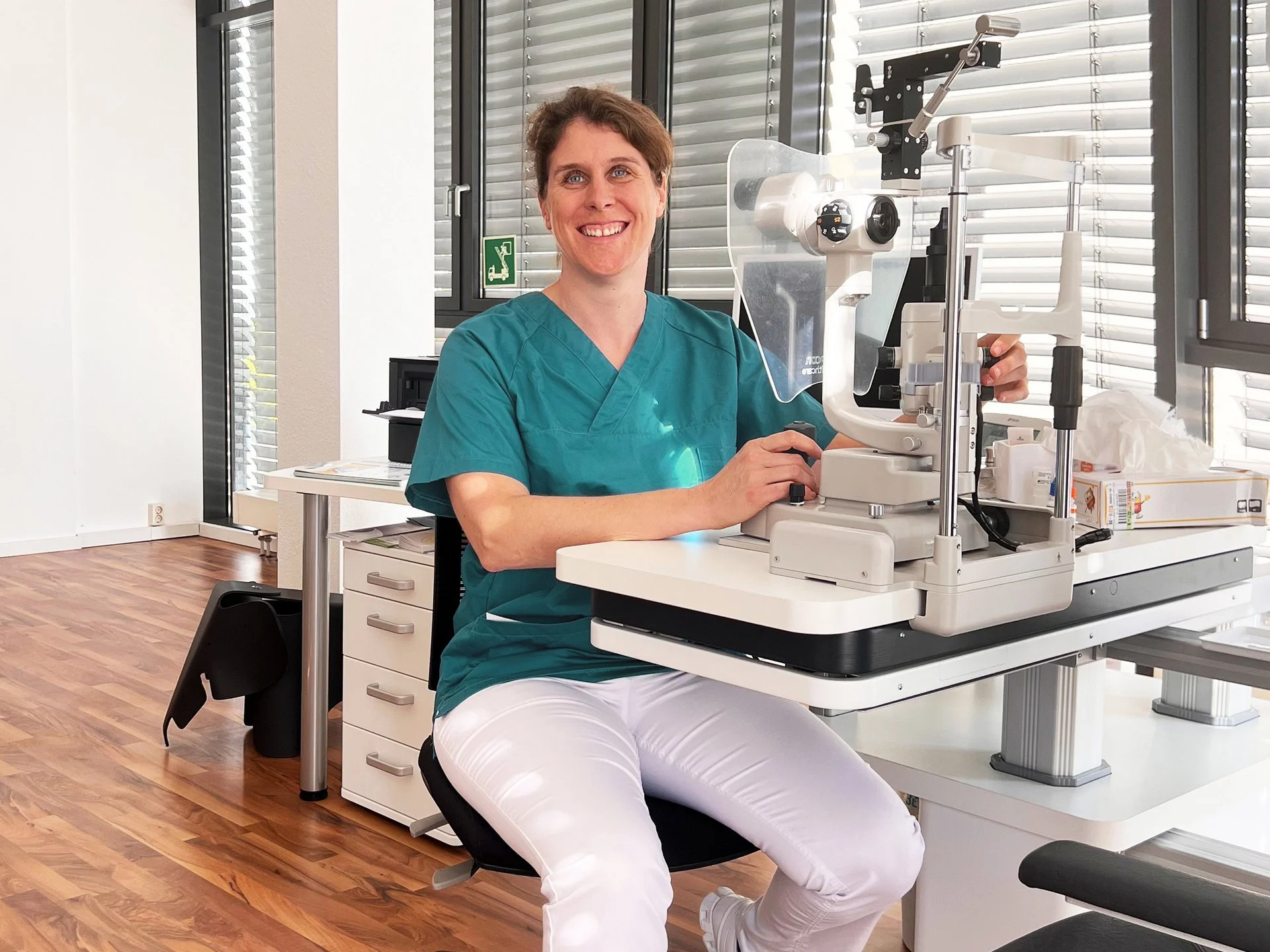 Eine Frau in medizinischer Kleidung arbeitet mit einem Ophthalmologie-Gerät in einem modernen Behandlungsraum.