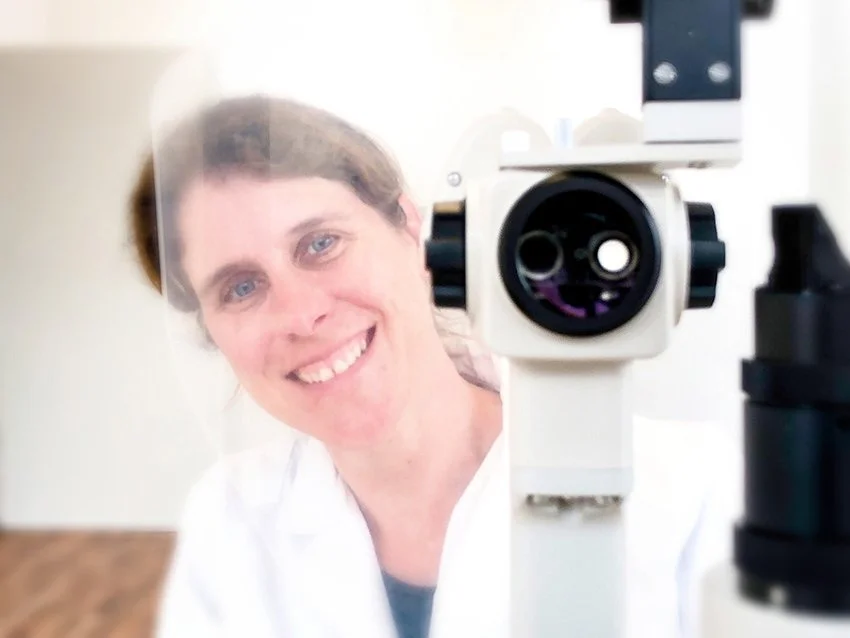 Lächelnde Frau in einem weißen Laborkittel hinter einem Mikroskop fotografiert