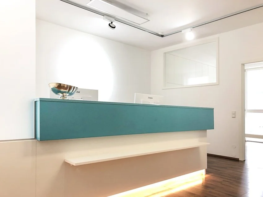 Rezeptionstresen in einem modernen, hellen Raum mit weißer Wand, Holzfußboden und einem Fenster