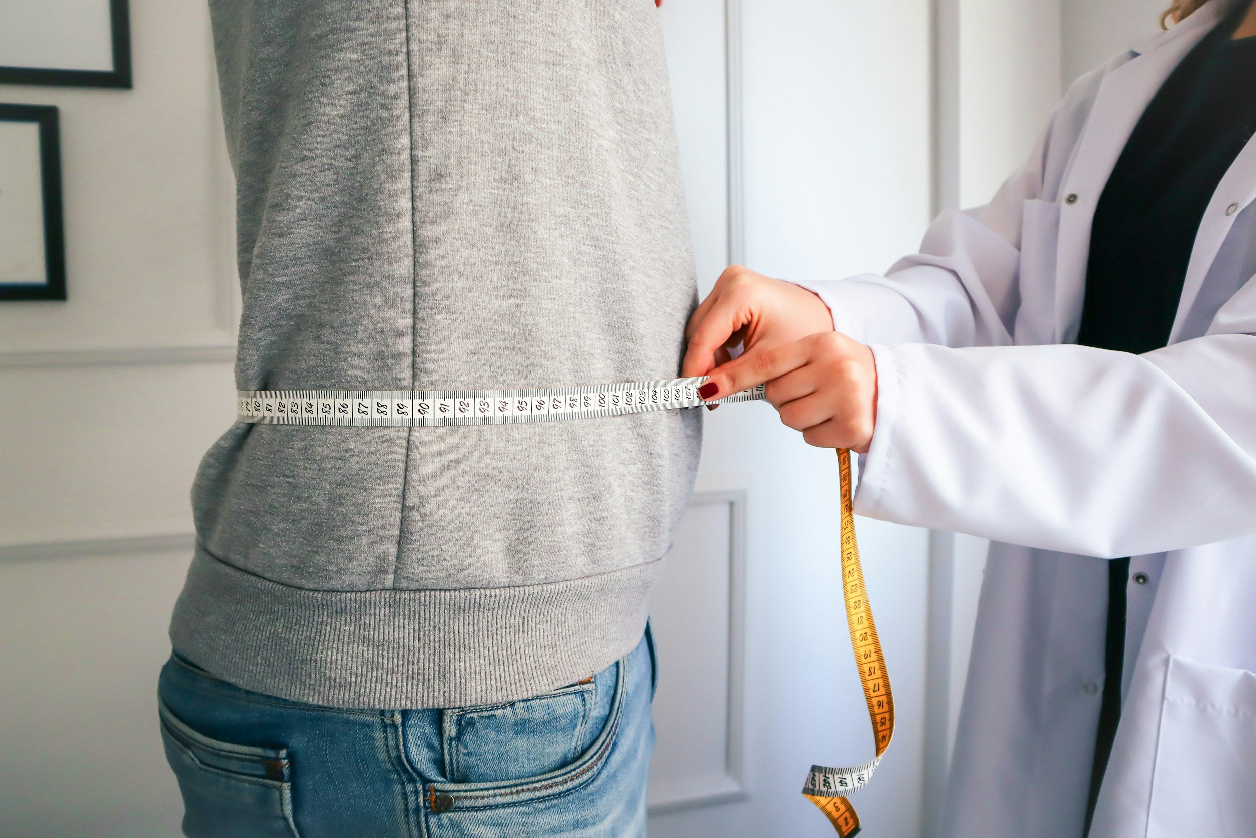 A healthcare professional using a measuring tape to measure a person's waist in a clinical setting.