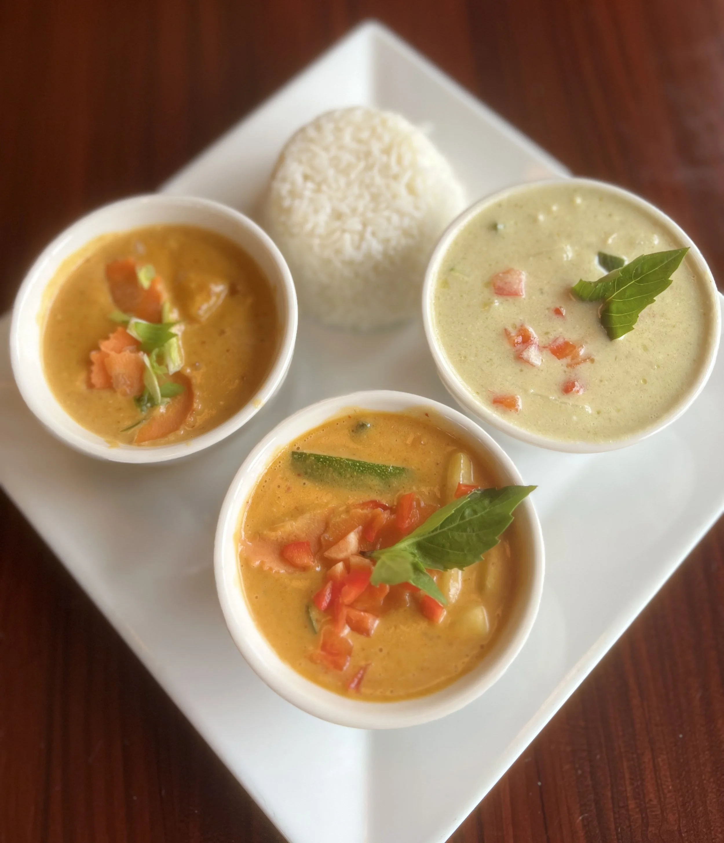 Indian meal with two bowls of curry, a bowl of coconut chutney, and a mound of white rice on a white plate