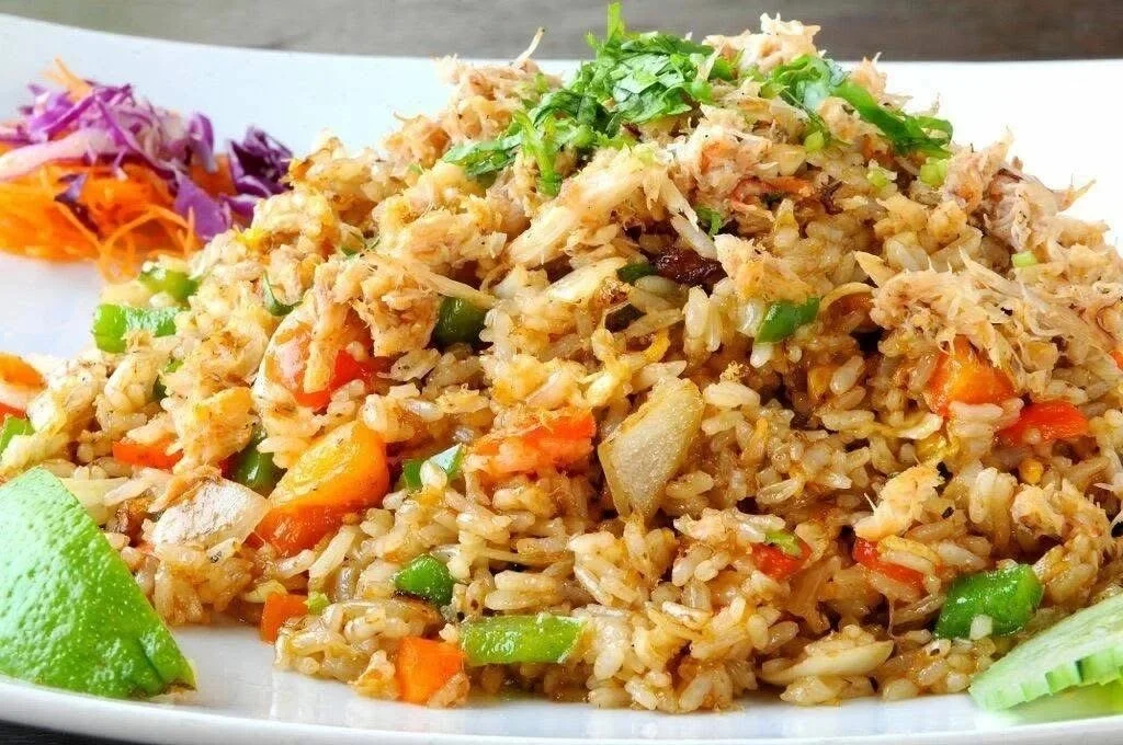 A plate of fried rice with vegetables like carrots, peas, and bell peppers, garnished with chopped herbs and lemon wedge, with some purple and orange shredded vegetables on the side.