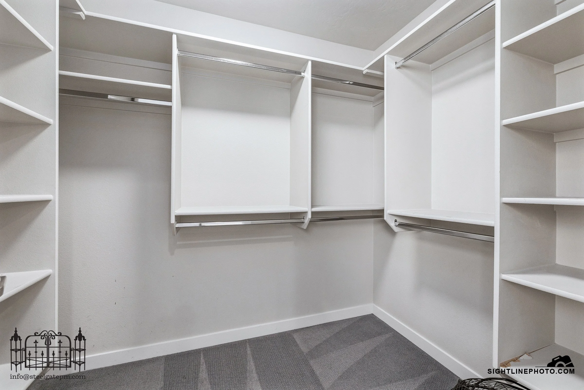 White empty walk-in closet with built-in shelves and hanging rods, gray carpeted floor.