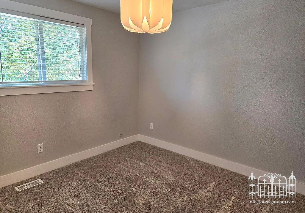 Empty bedroom with gray walls, carpeted floor, window with blinds, and a ceiling light fixture.