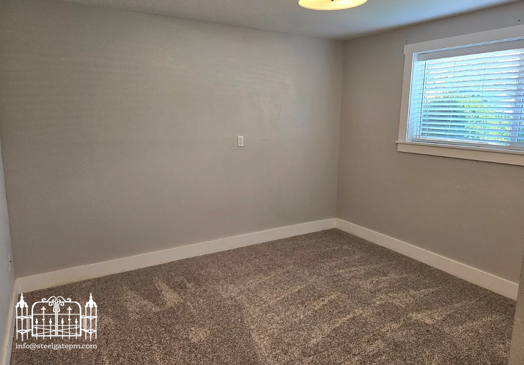 Empty room with beige walls, carpeted floor, a window with blinds, and a ceiling light fixture.