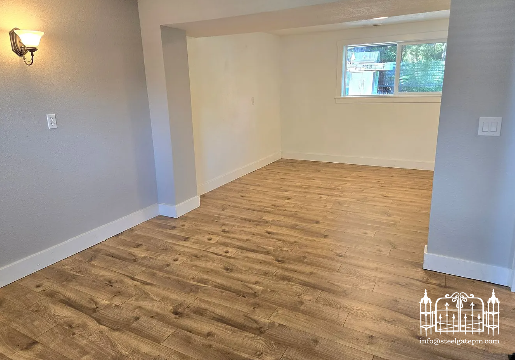 Empty room with light-colored walls, wood flooring, and a window showing outdoor scenery.
