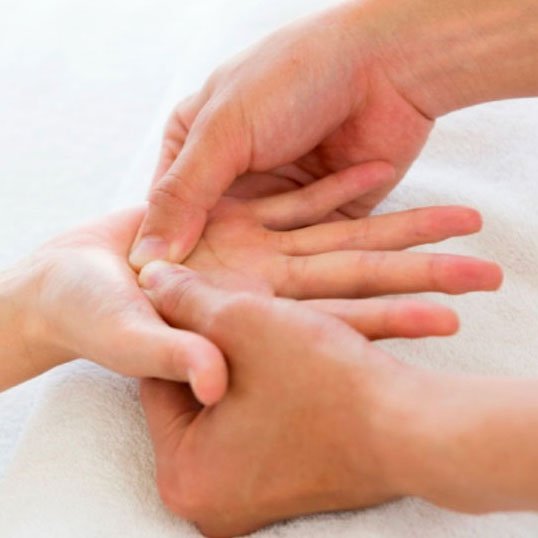 A close-up of a massage therapist's hands applying pressure to a person's hand for a massage.