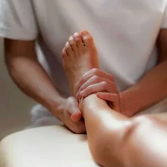 Person lying on a bed with a healthcare professional or massage therapist holding their foot.