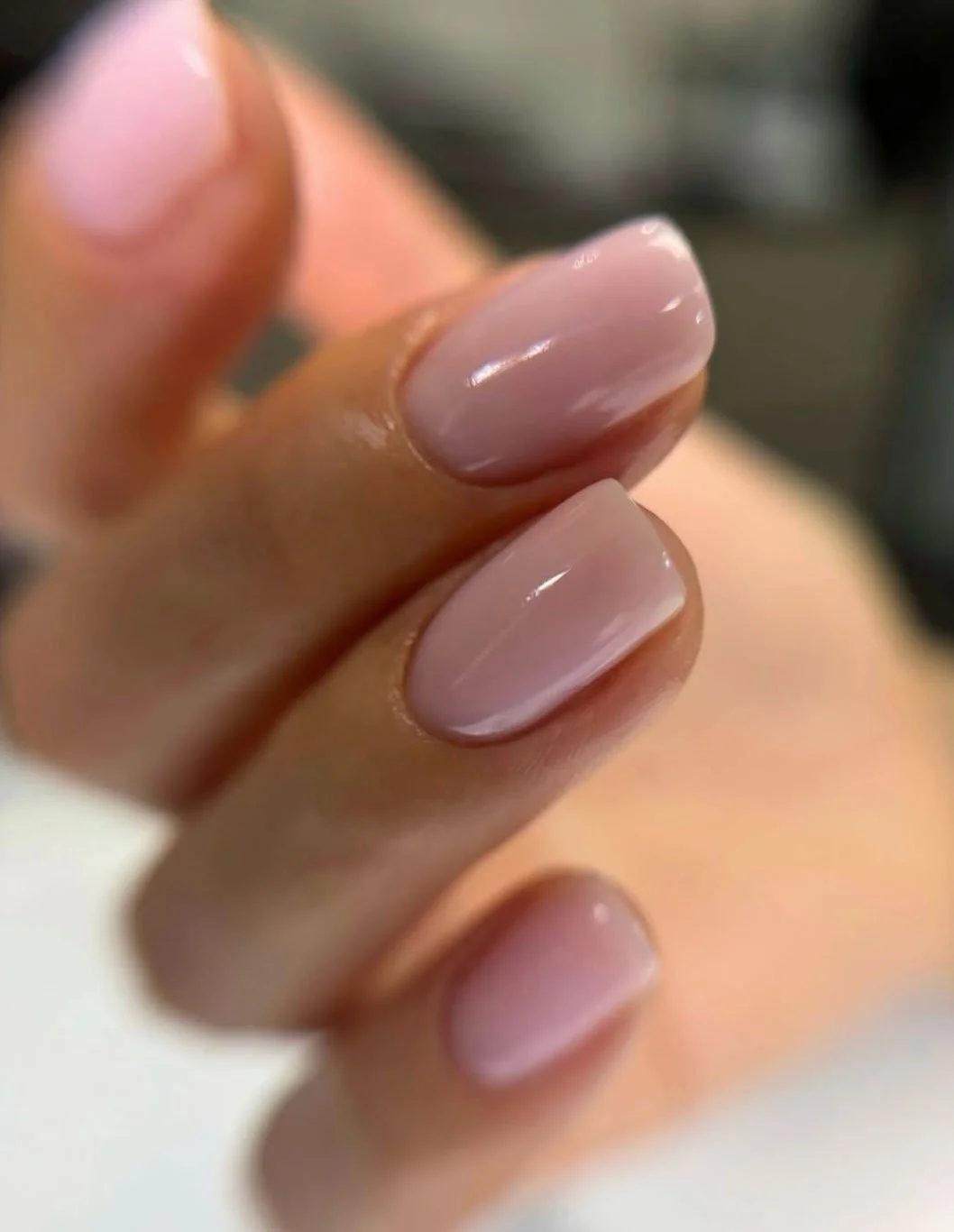 Close-up of a person's fingers showing a fresh, shiny manicure with natural pinkish-nude nails.