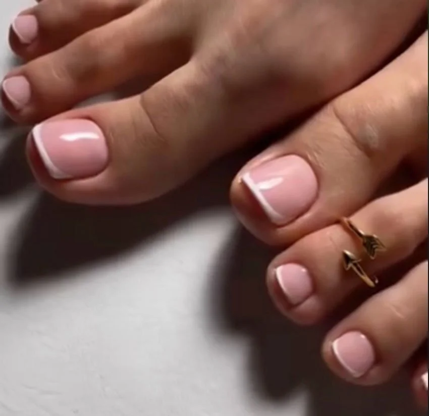 Close-up of a hand with manicured nails and a gold arrow-shaped ring on the finger.