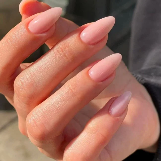 Close-up of five fingers with long, oval-shaped, nude-colored acrylic nails.