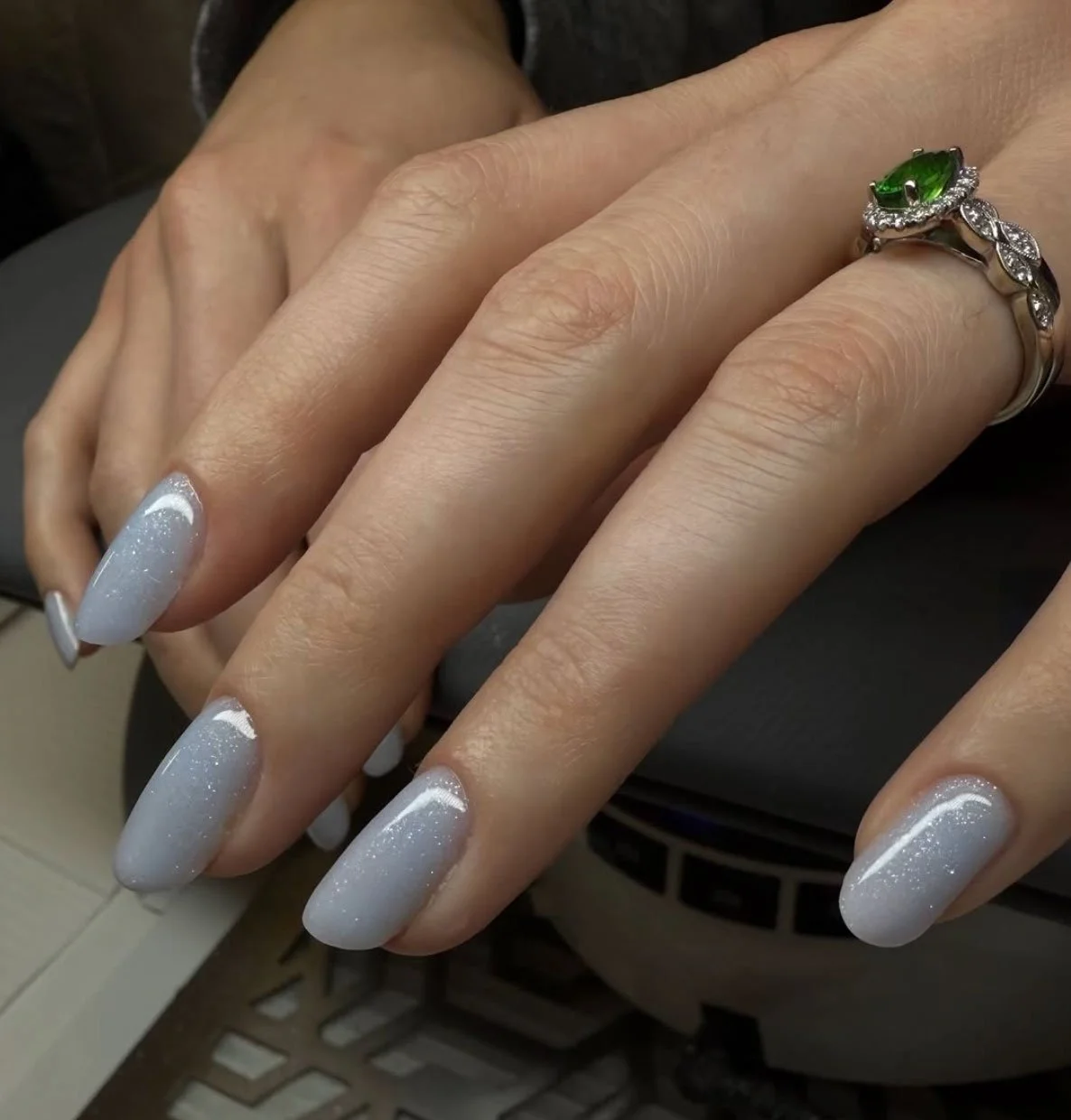 Close-up of a woman's hands with manicured nails and a silver ring with a green gemstone.