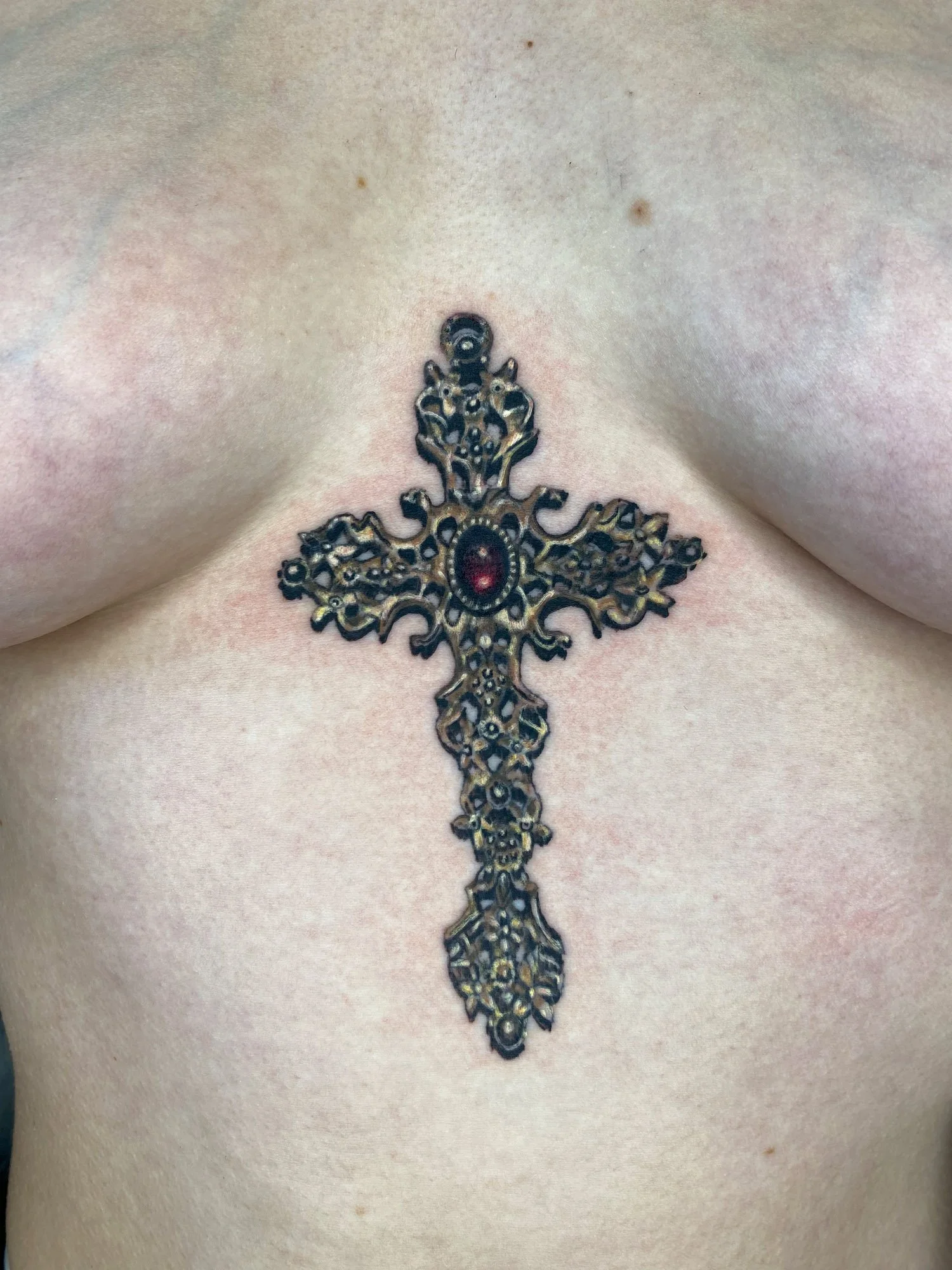 Close-up of a decorative metal cross tattooed on a person's chest.