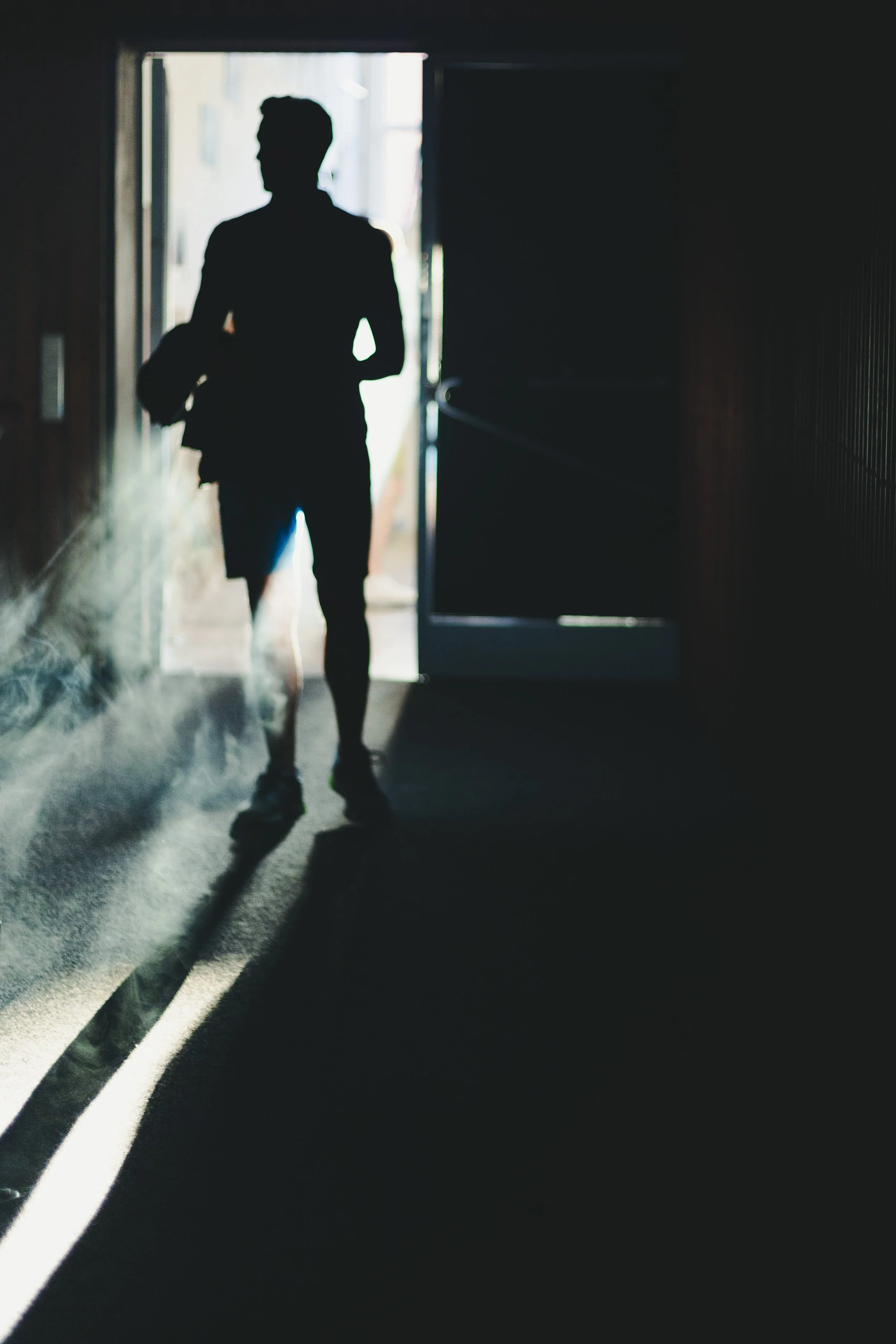 Silhouette eines Mannes mit Rucksack, der durch eine Tür in einen hell erleuchteten Raum geht.