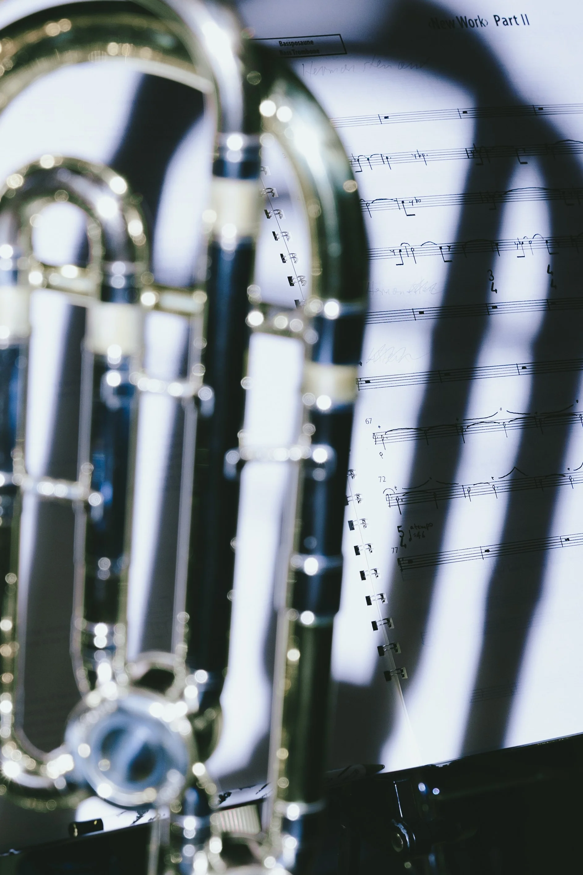 Detail eines silbernen Musikinstrumentes vor einem Notenblatt mit Musiknoten in Schattenwurf.