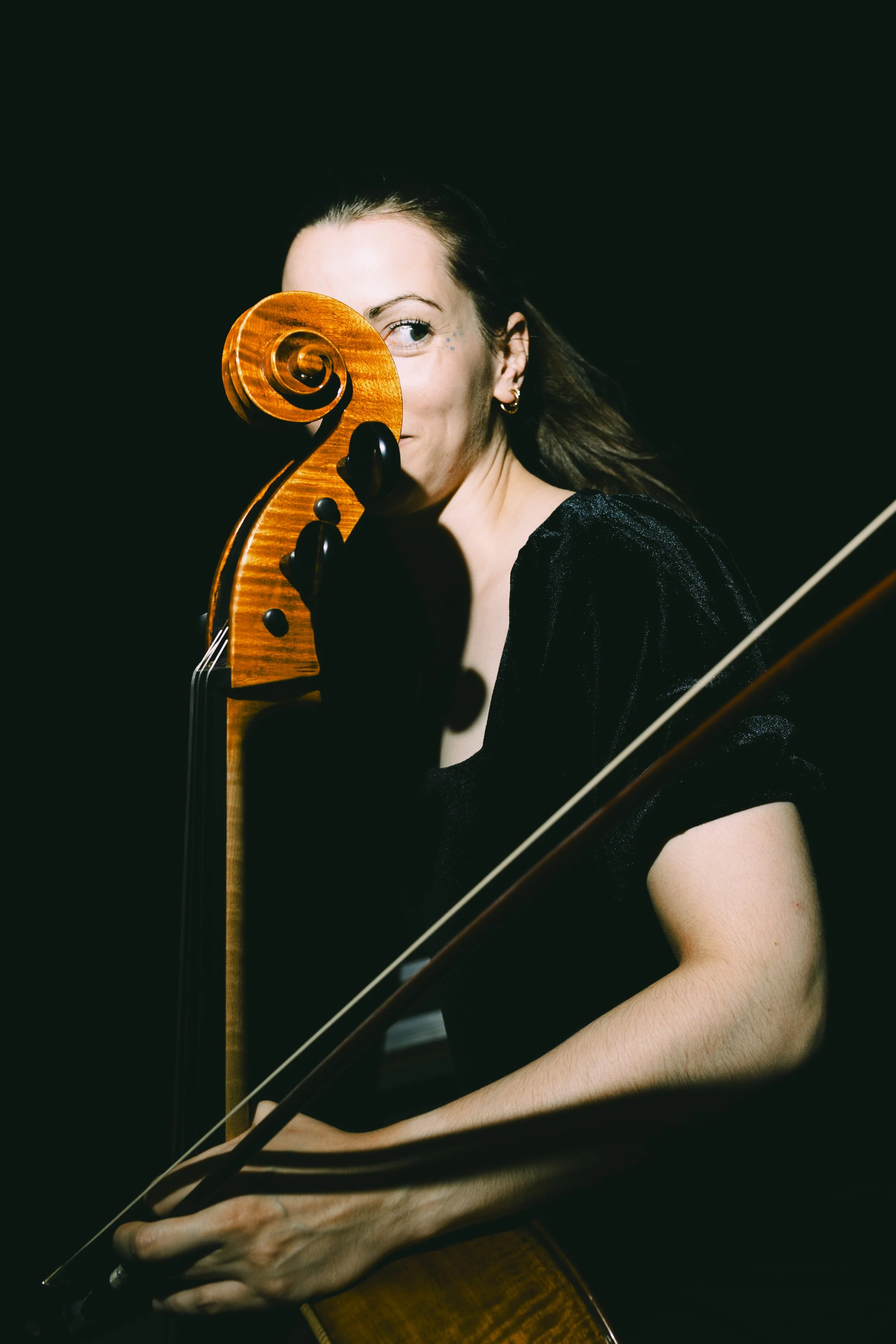 Junge Frau spielt Geige, mit einem Spiralholz vor einem schwarzen Hintergrund.