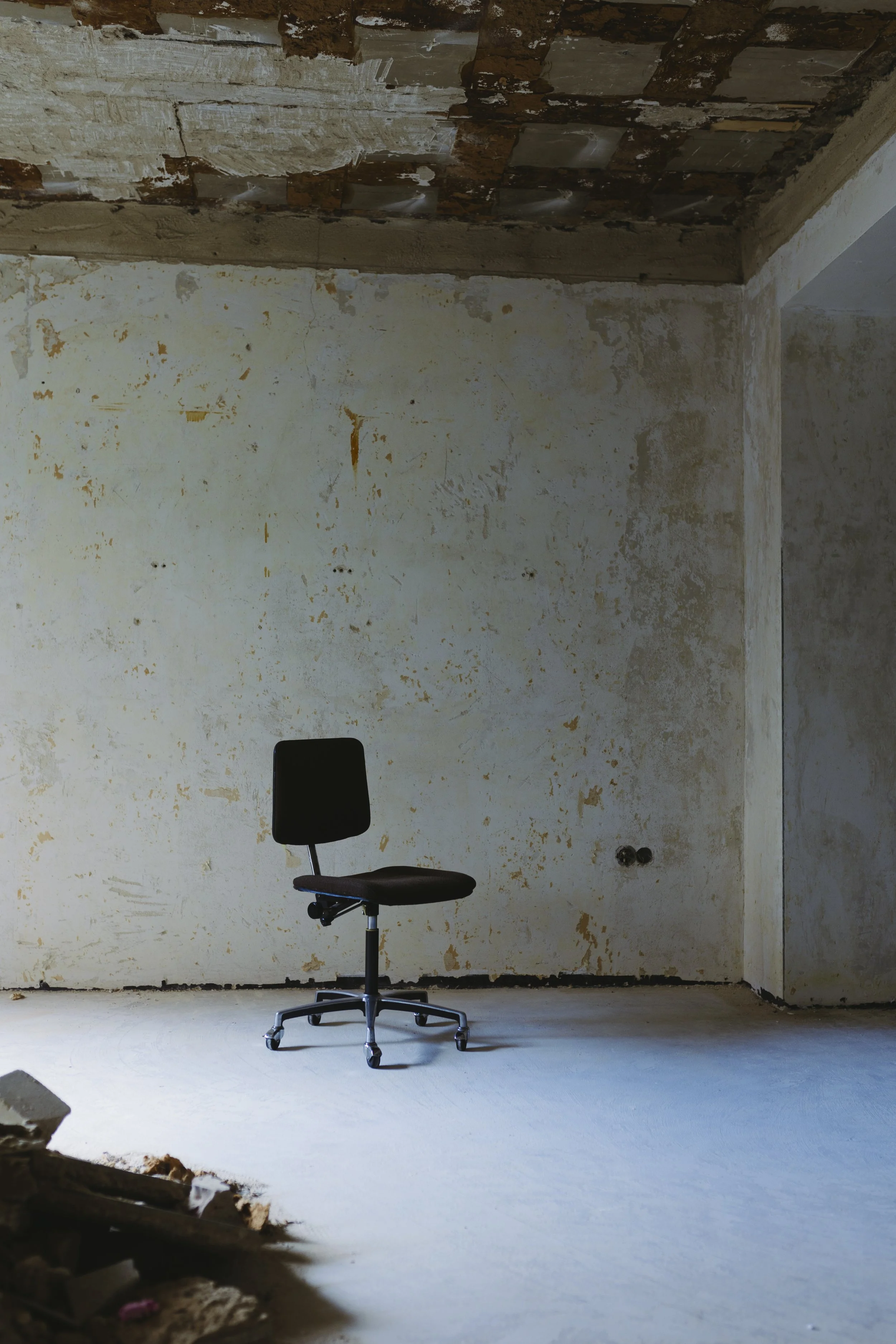 Ein einzelner schwarzer Bürostuhl in einem unfertigen, unbewohnten Raum mit rohen Wänden und einem unvollständigen Decke, der vermutlich im Bau ist.