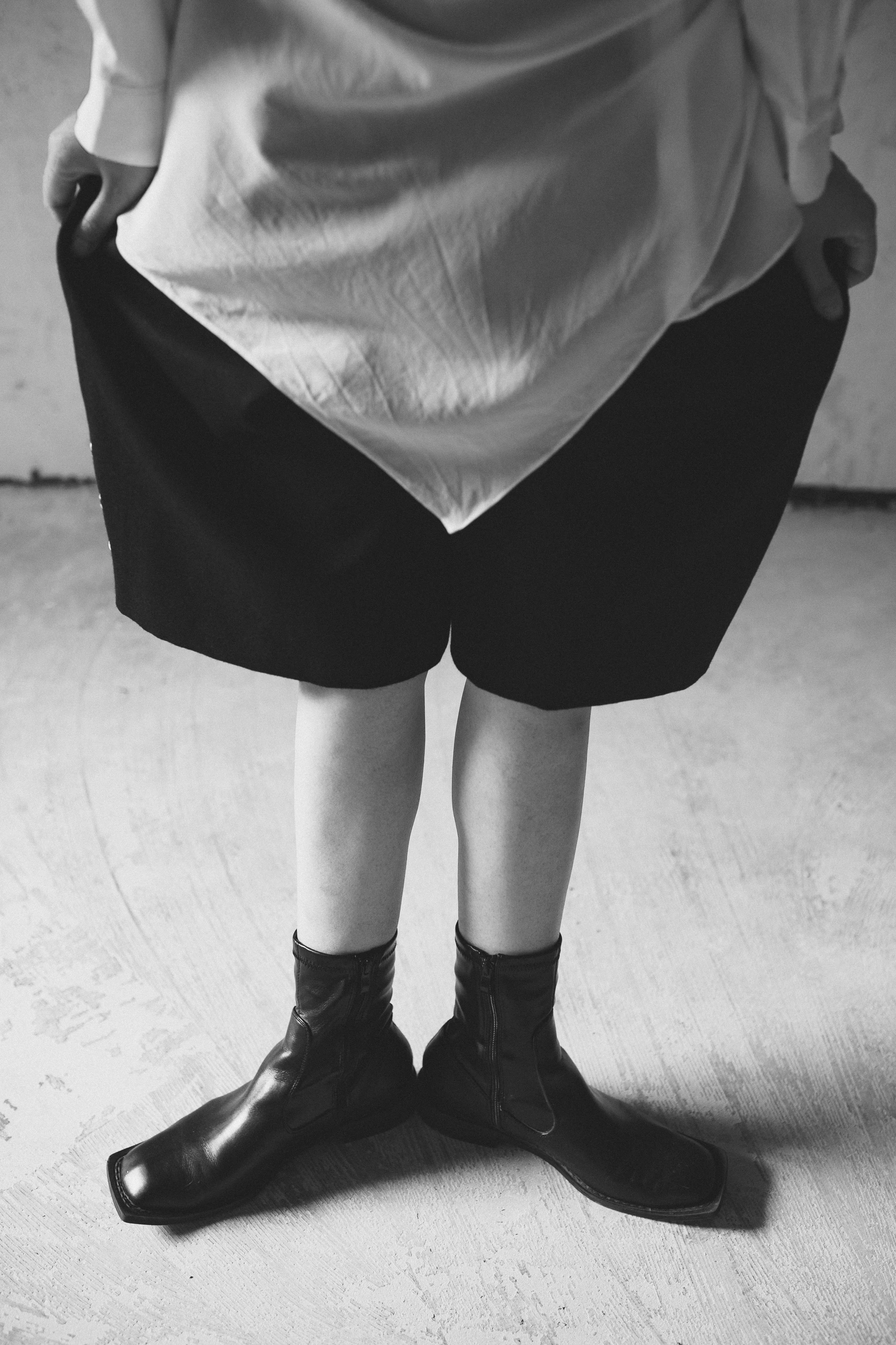 Nahaufnahme von einer Person, die schwarze Stiefel trägt, mit einem schwarzen Rock und einem hellen Oberteil. Die Person steht auf einem Holzboden.