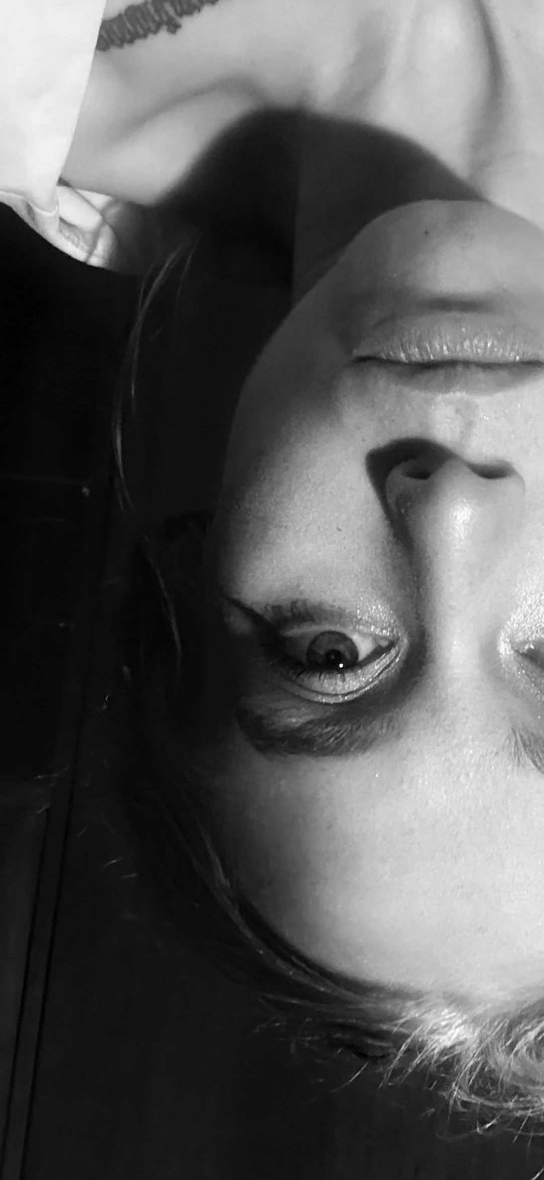 A black-and-white close-up photo of a woman's face, emphasizing her nose and lips, with her eye visible in the lower part of the image.