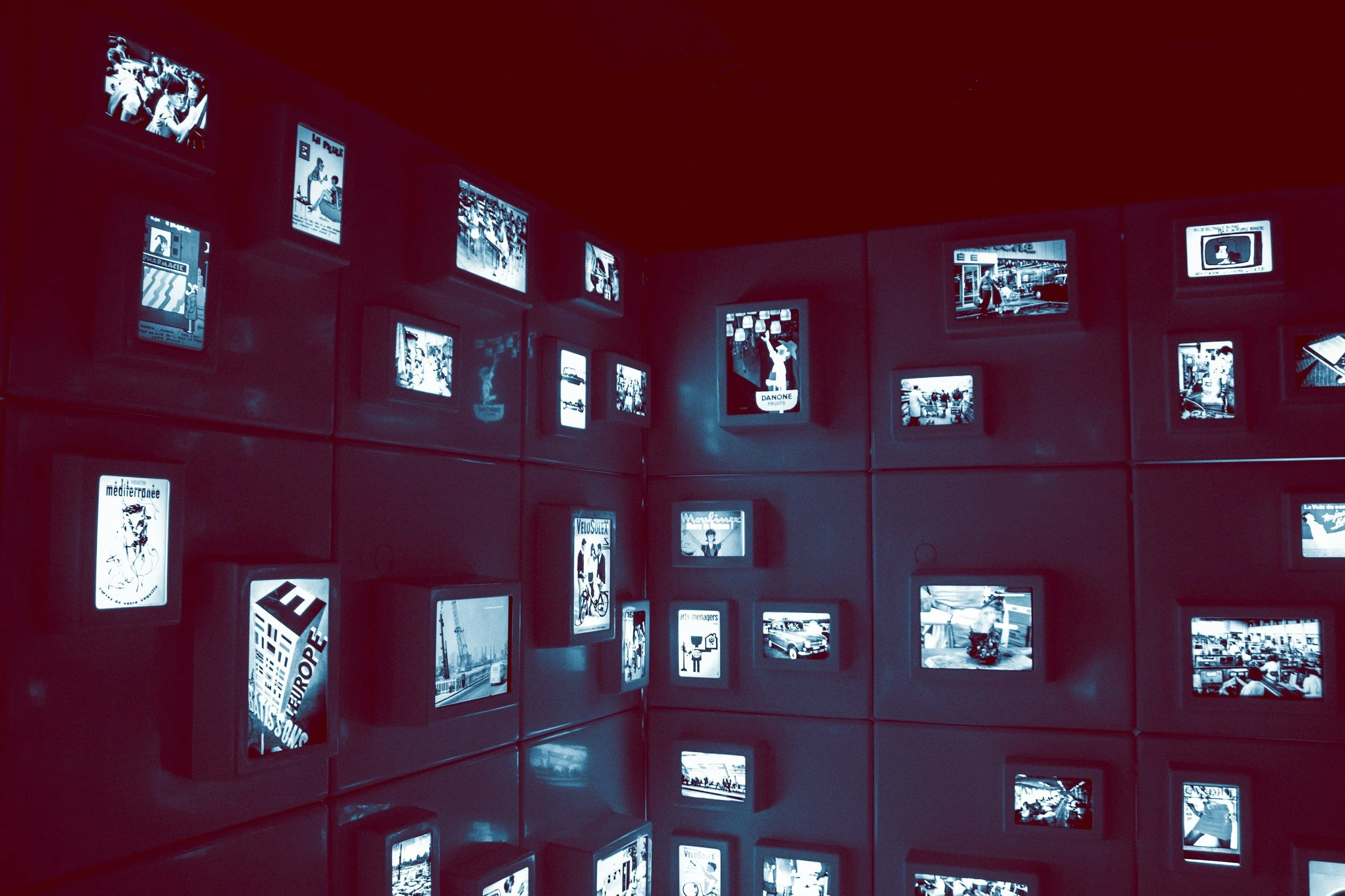 Wall with multiple small illuminated screens showing various black-and-white images and illustrations.