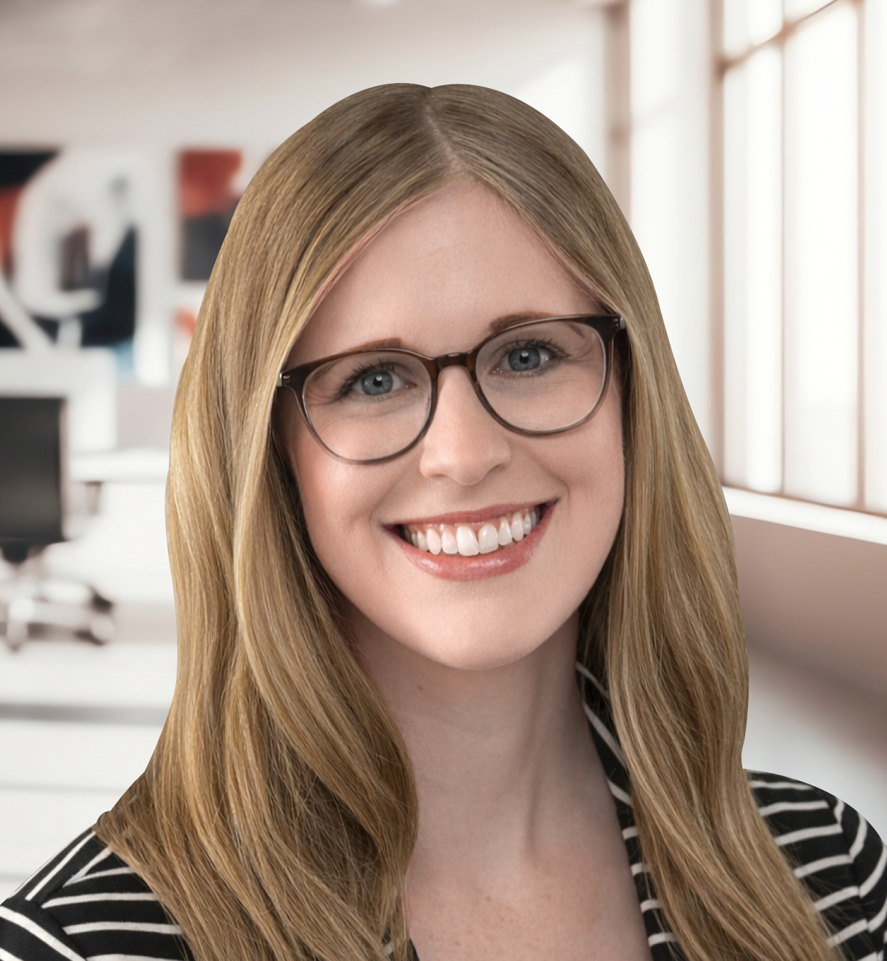 Smiling woman with long blonde hair, wearing glasses and a black and white striped top, in an office setting with blurred background of desks and large windows.