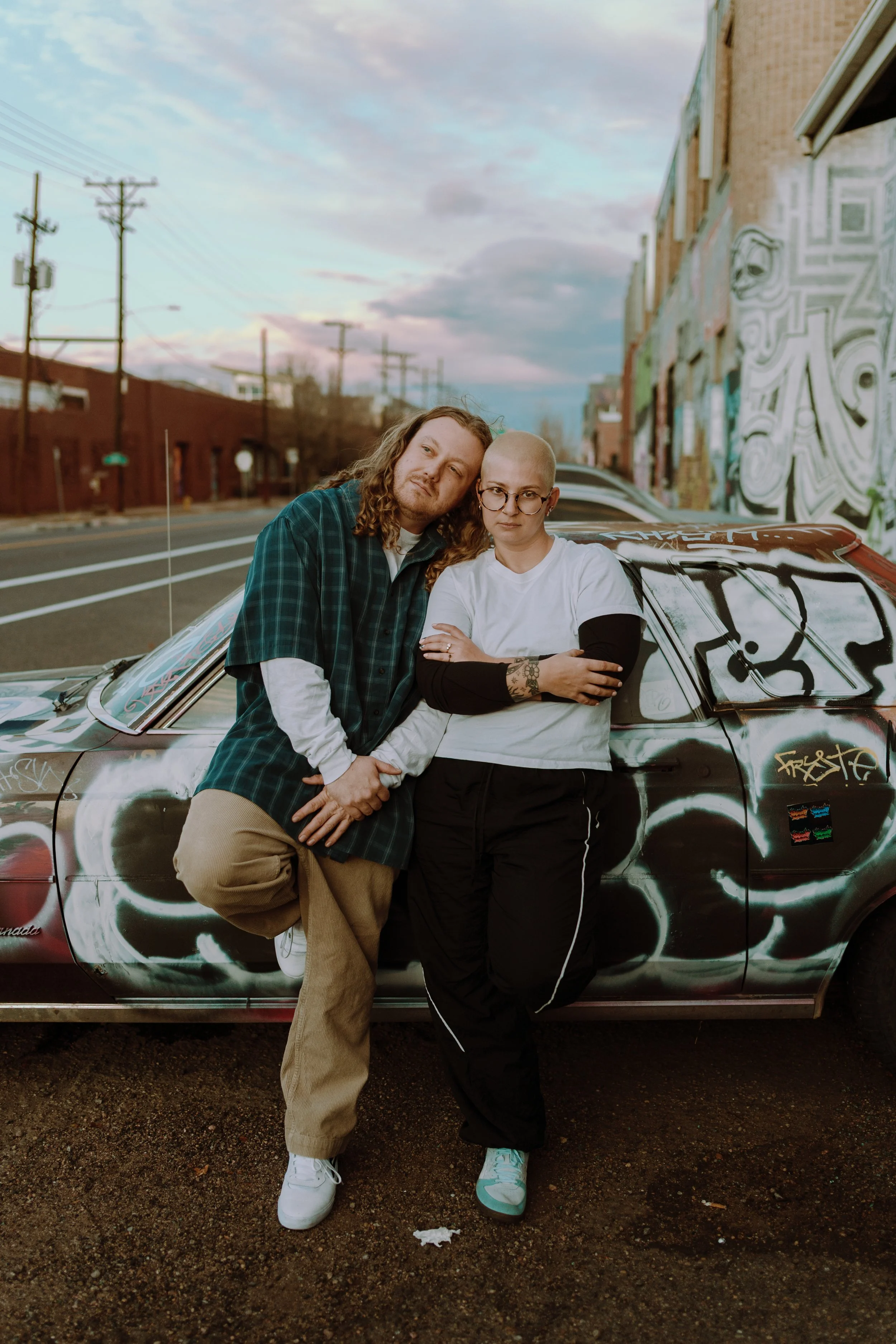 Engagement photo with Anna and Ryder standing in front of a graffitied car.