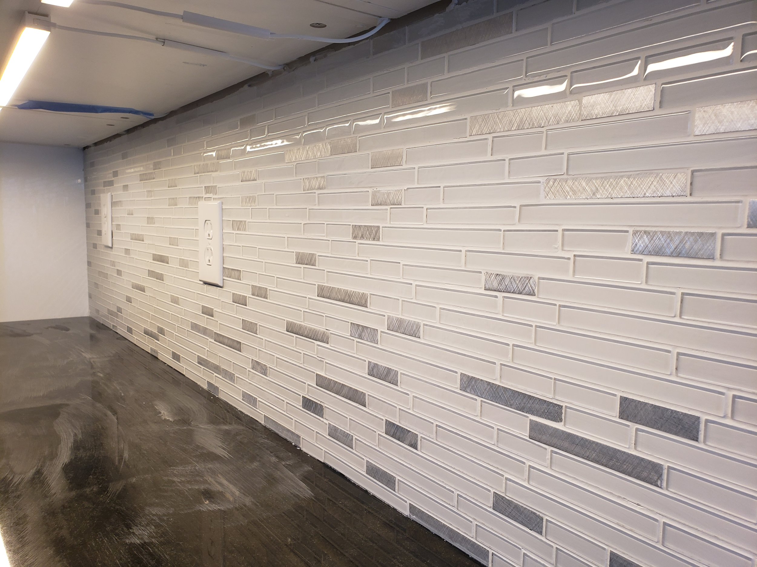 Interior wall with white subway tiles and electrical outlets, under construction lighting, dark wooden floor.