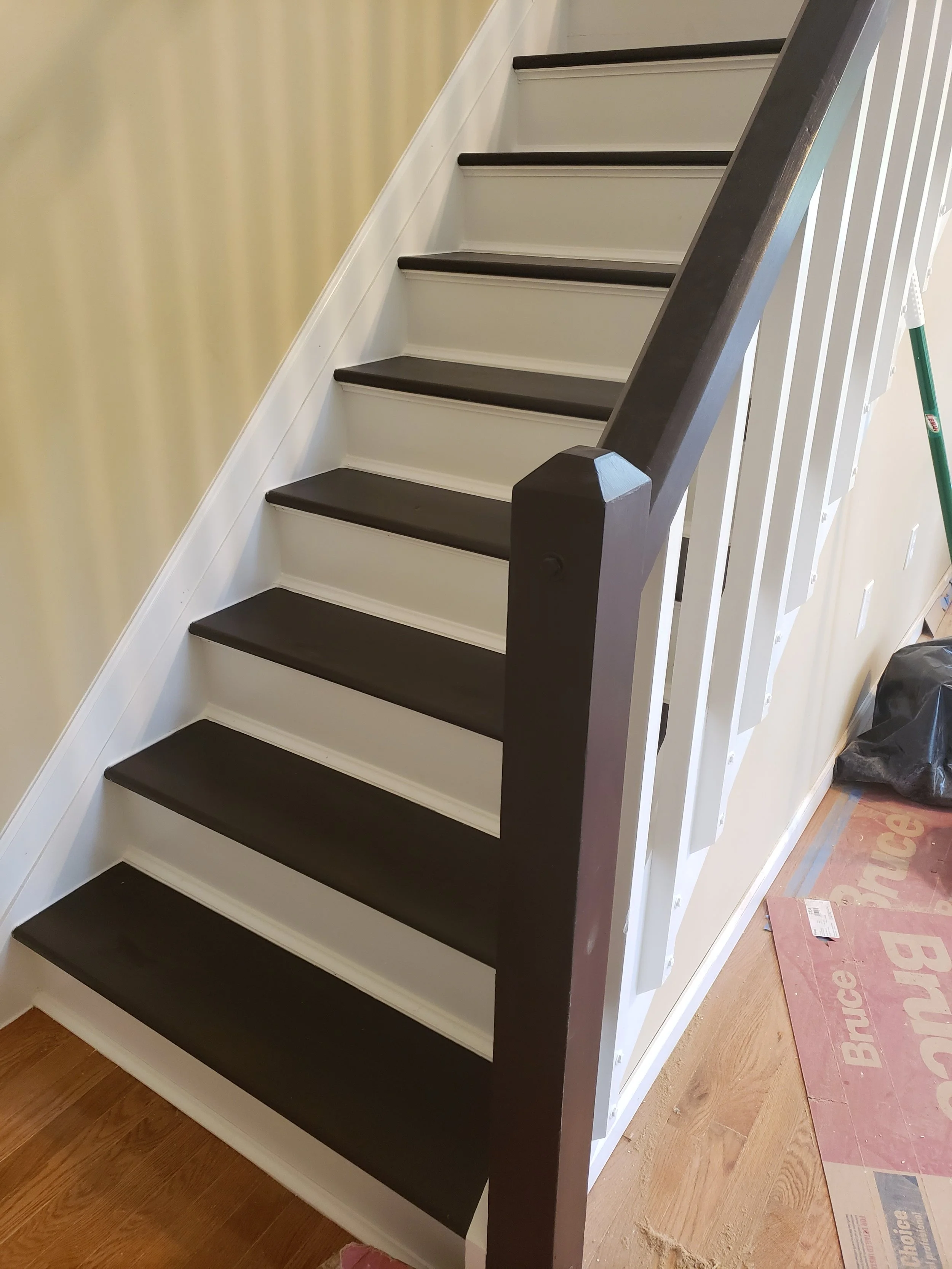 Inside view of a staircase with black treads, white risers, white side panels, and a dark brown handrail.