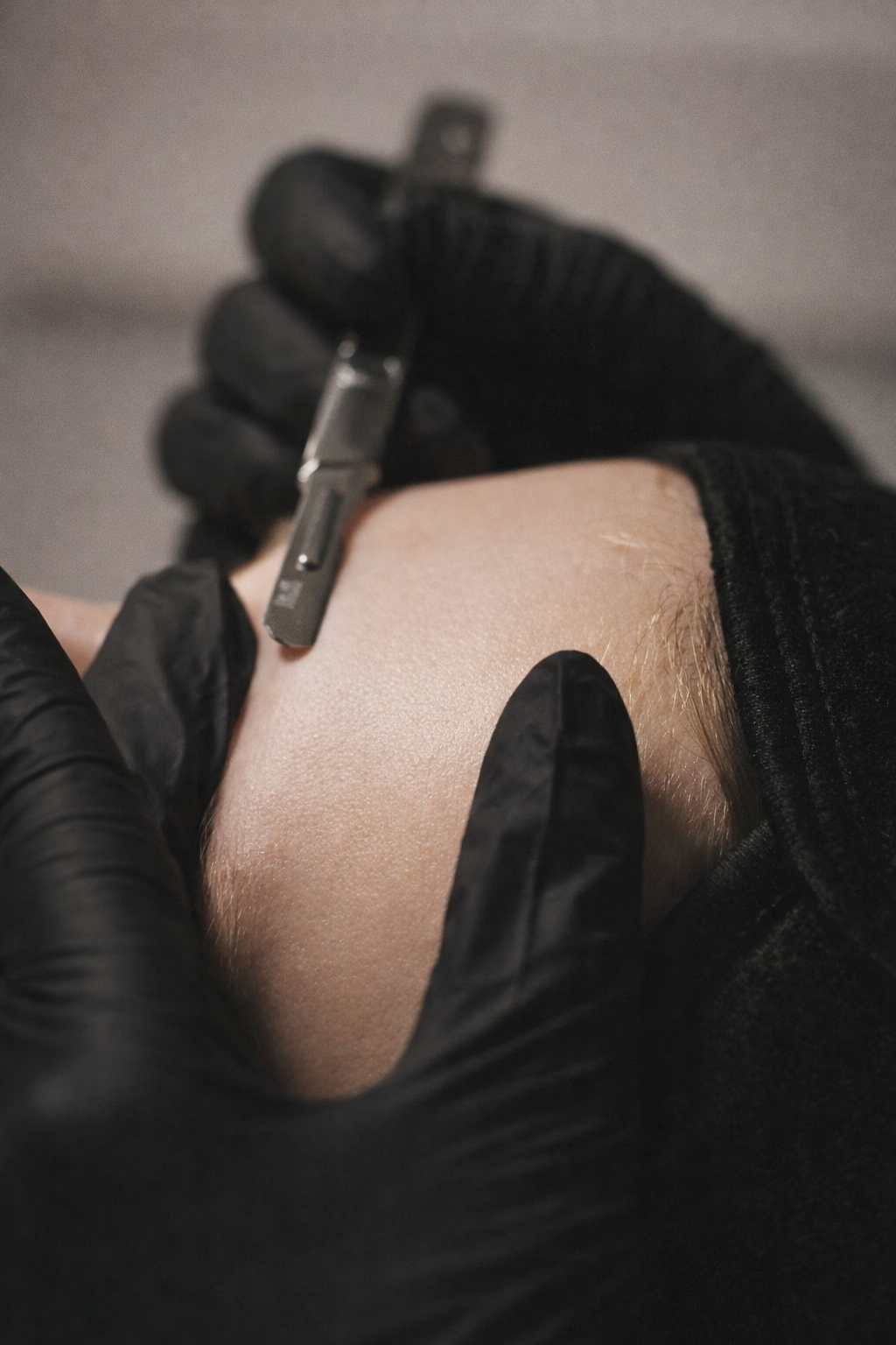 A person wearing black gloves receiving a tattoo on their forearm with a tattoo machine.