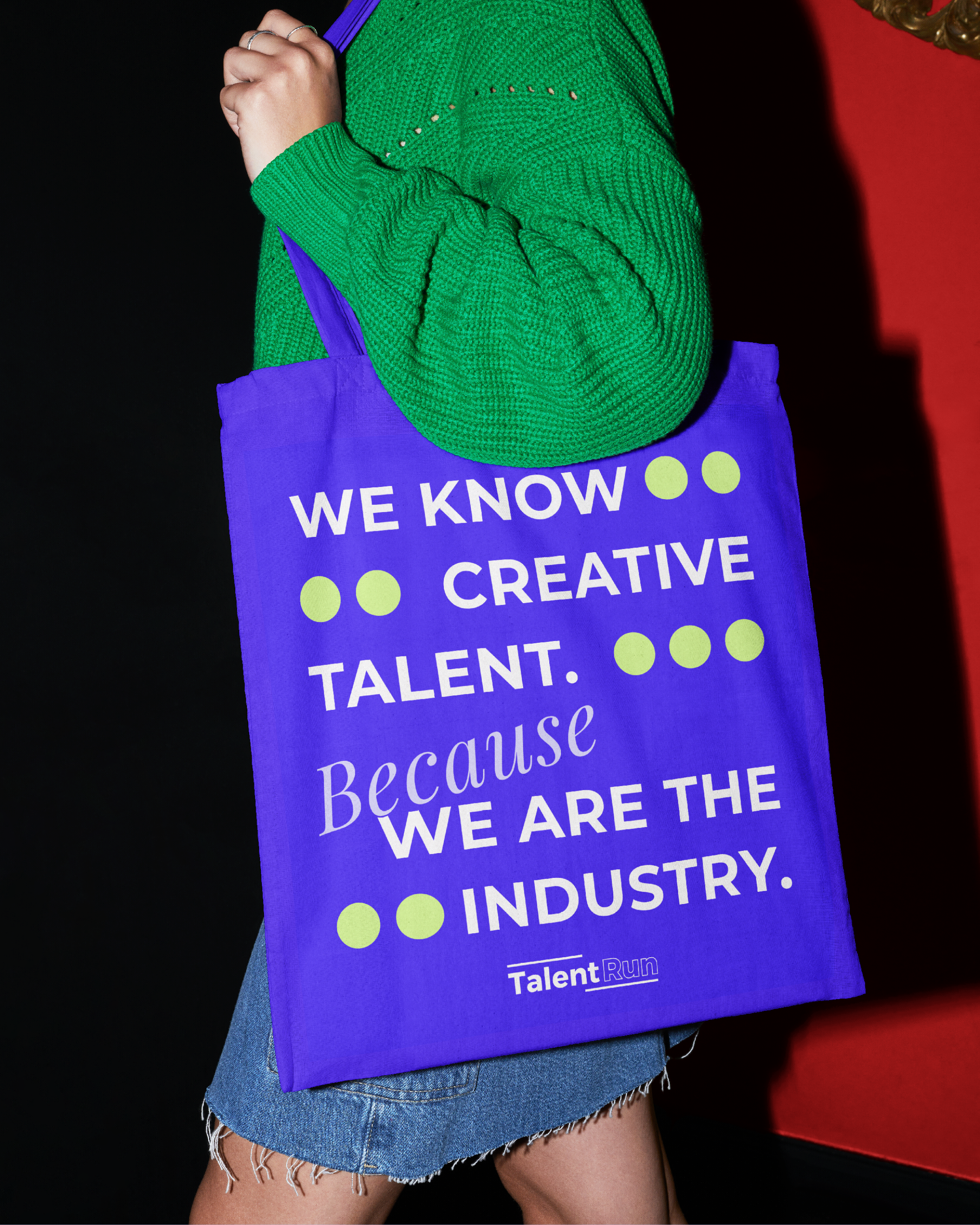 Person carrying a purple bag with the quote 'We know creative talent. Because we are the industry.' in bold, white, and purple text, over a green sweater and denim shorts, against a black and red background.
