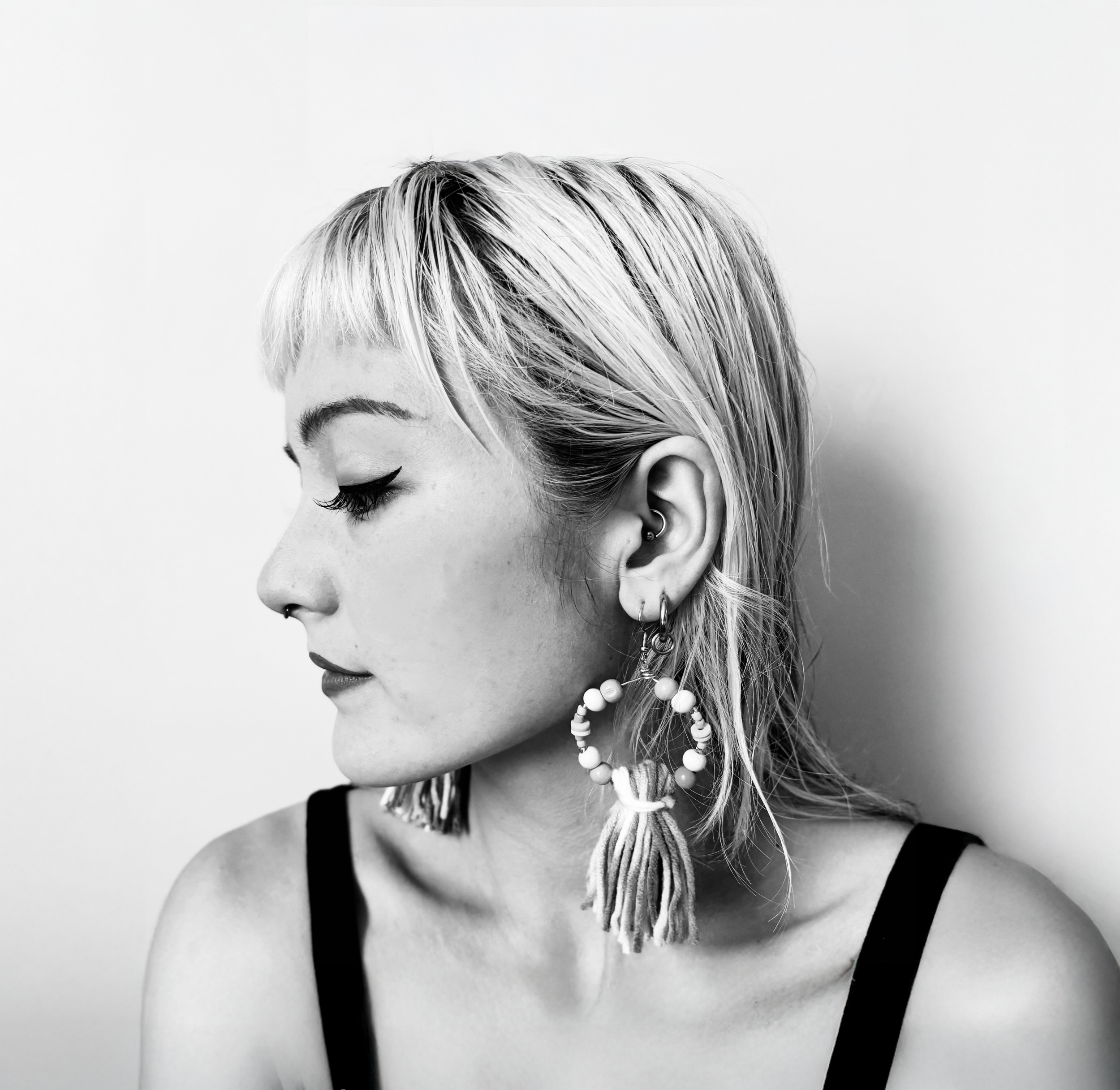 Side profile of a woman with short blonde hair, wearing tassel earrings and a black sleeveless top.