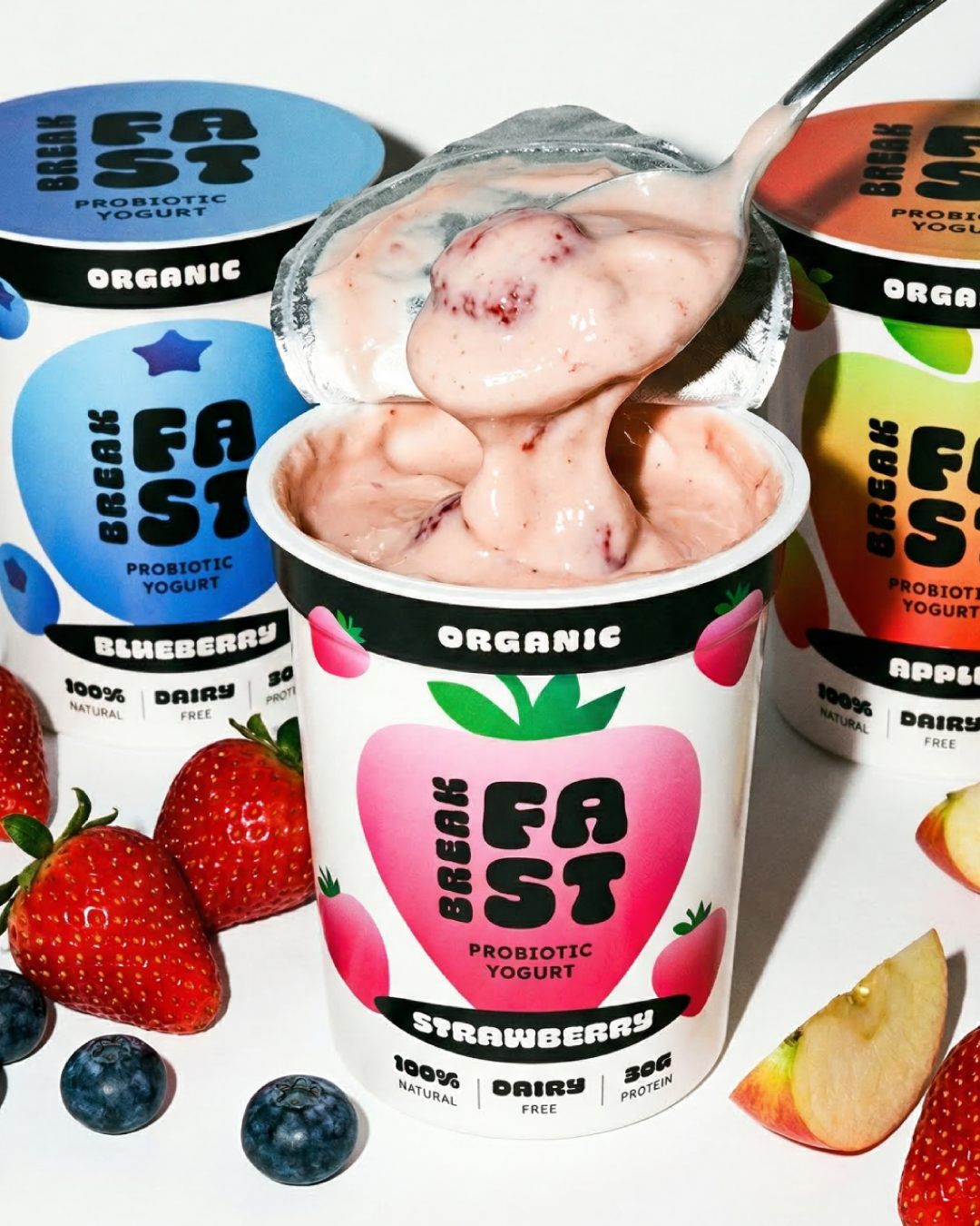 Open container of strawberry probiotic yogurt with spoon, surrounded by strawberries and blueberries.