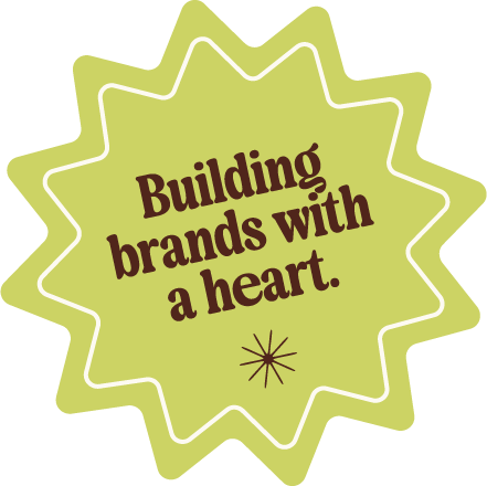 A lime-green badge with white outline, containing the text 'Building brands with a heart' in brown, and a small decorative star-like symbol underneath.
