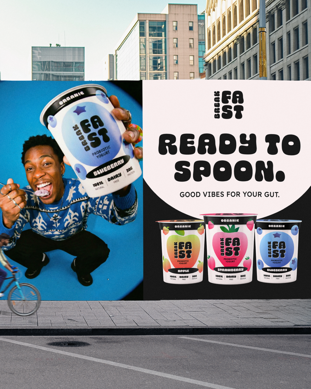 Advertisement billboard for Beach Fask probiotic yogurt in an urban setting featuring a smiling young man with rings on his fingers holding a Blueberry flavored yogurt cup, with the slogan 'Ready to Spoon' and images of yogurt cups flavored apple, strawberry, and blueberry.