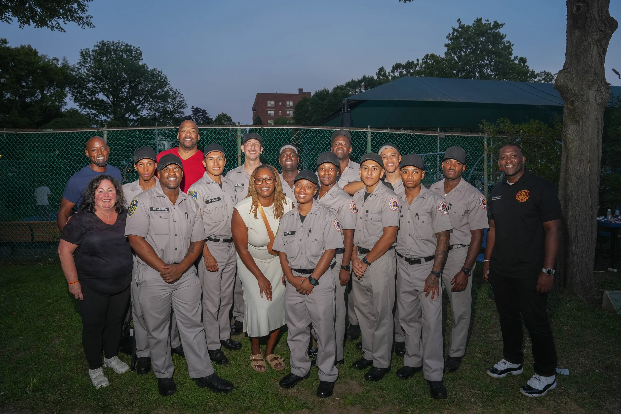 Group photo of police officers and community members outdoors, smiling at the camera during evening.