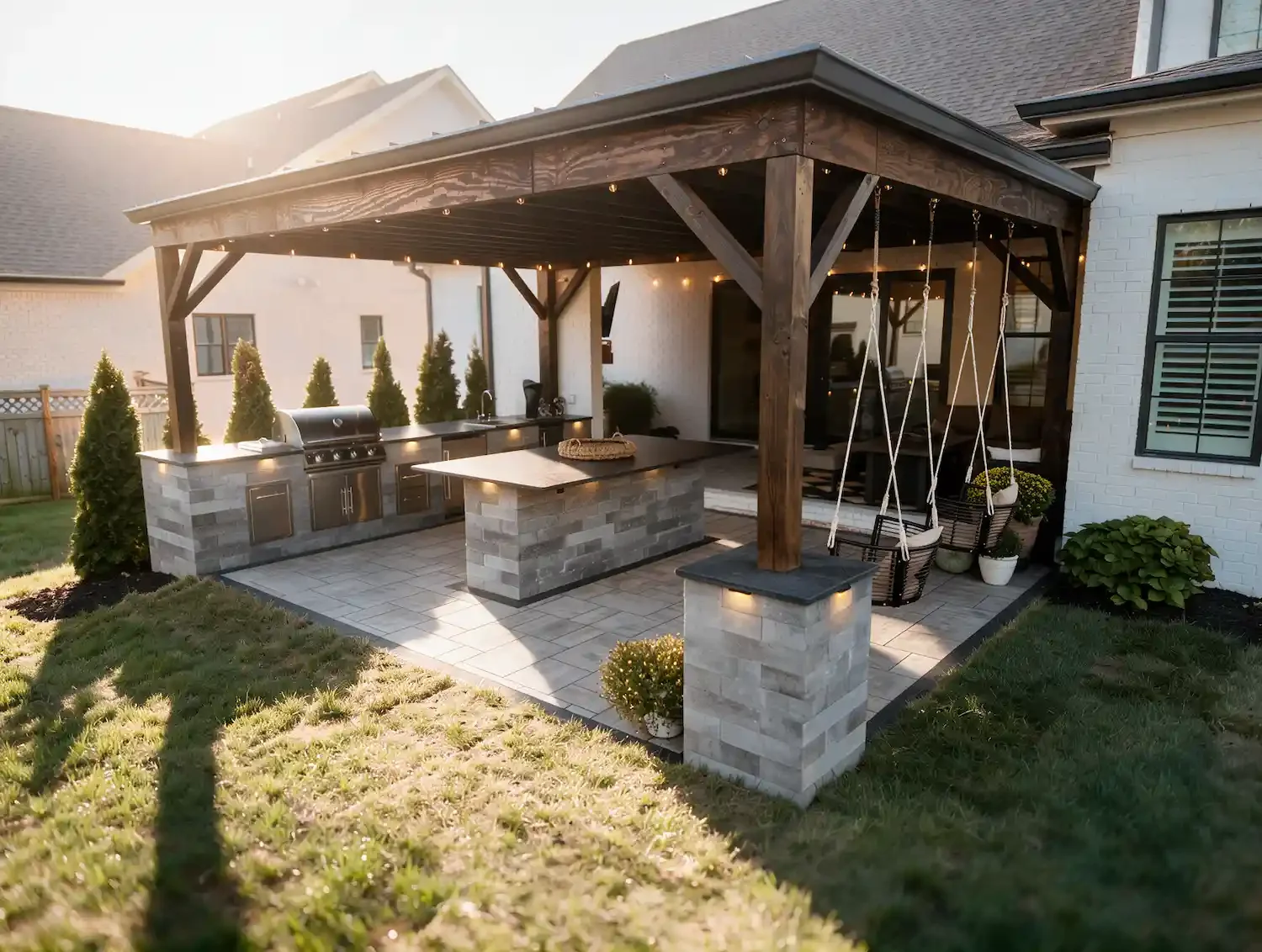 Covered outdoor kitchen patio with grill, island, string lights, and two swing chairs