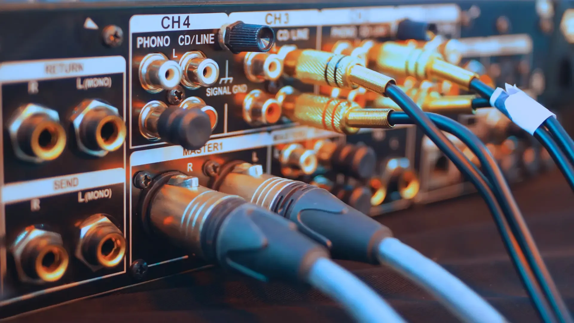 Close-up of an audio mixer with multiple RCA cables plugged into various input channels.