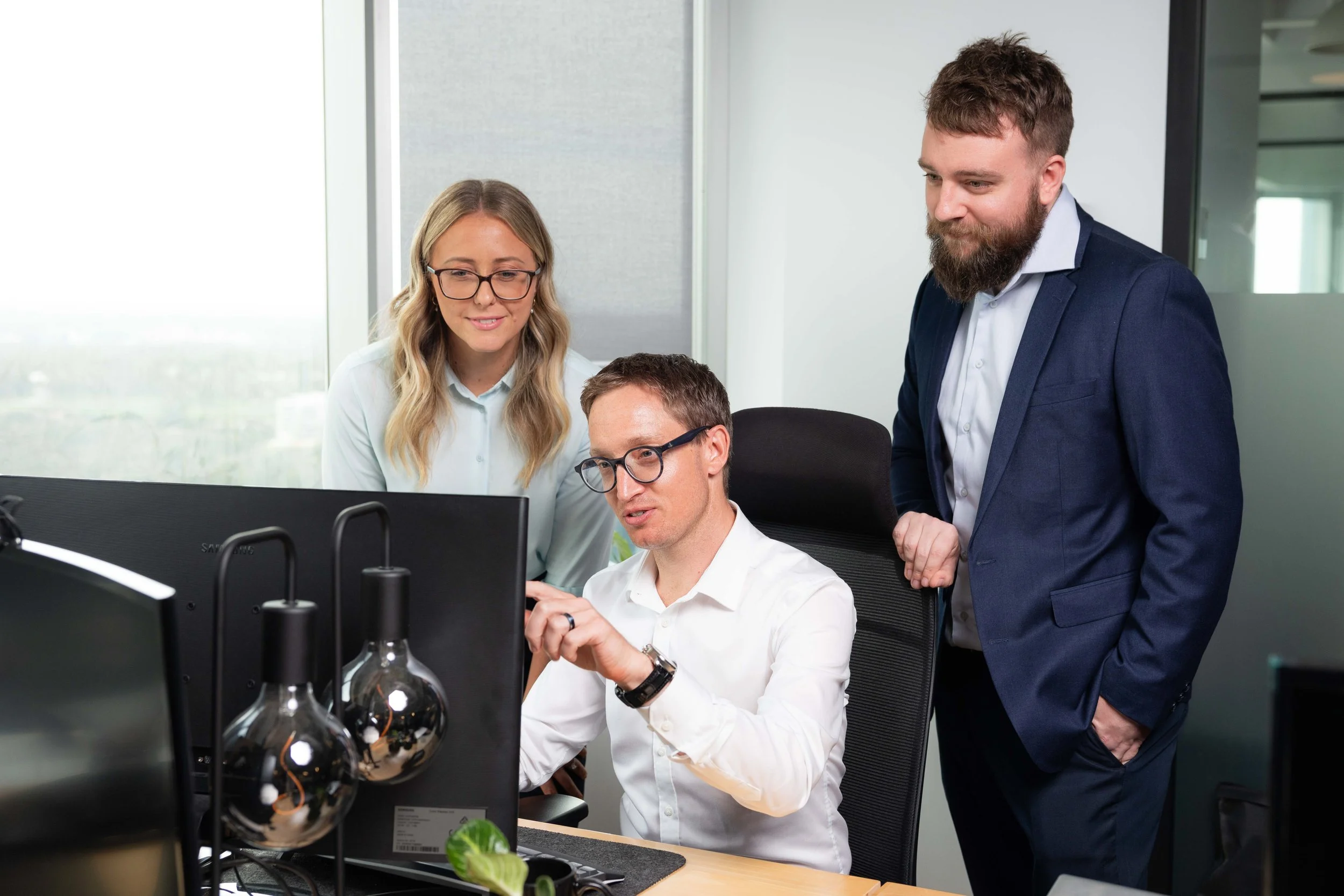Three professionals in an office, gathered around a computer, discussing work.