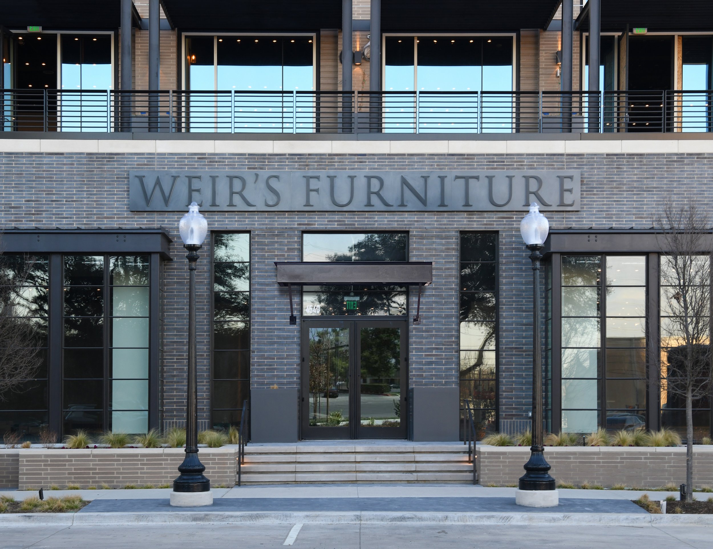 Exterior view of a two-story modern furniture store named Weir's Furniture with large windows, a brick facade, and two vintage-style street lamps in front.