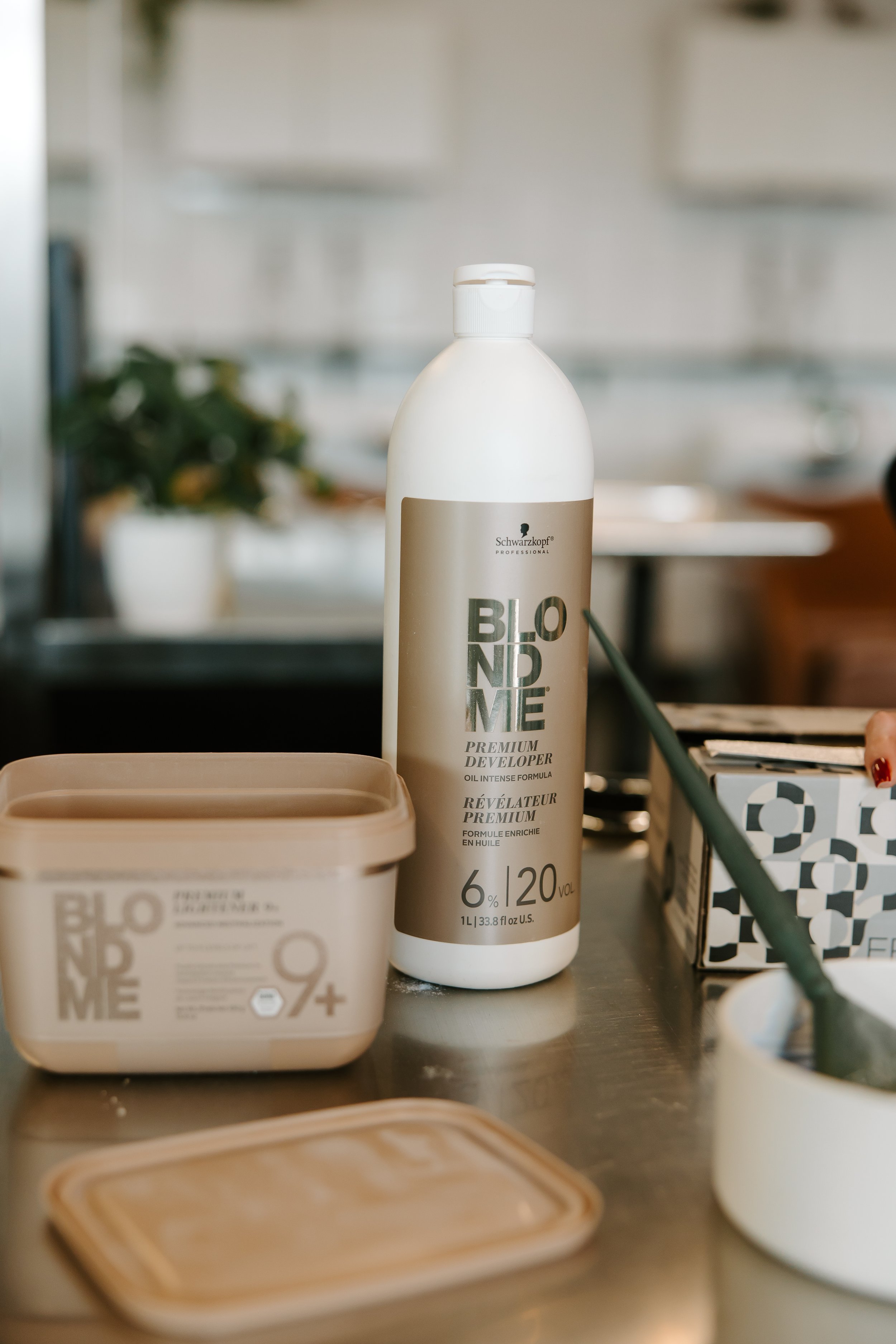 A bottle of Schwarzkopf Professional Blond Me Premium Developer hair dye standing on a kitchen counter surrounded by hair coloring supplies and containers.