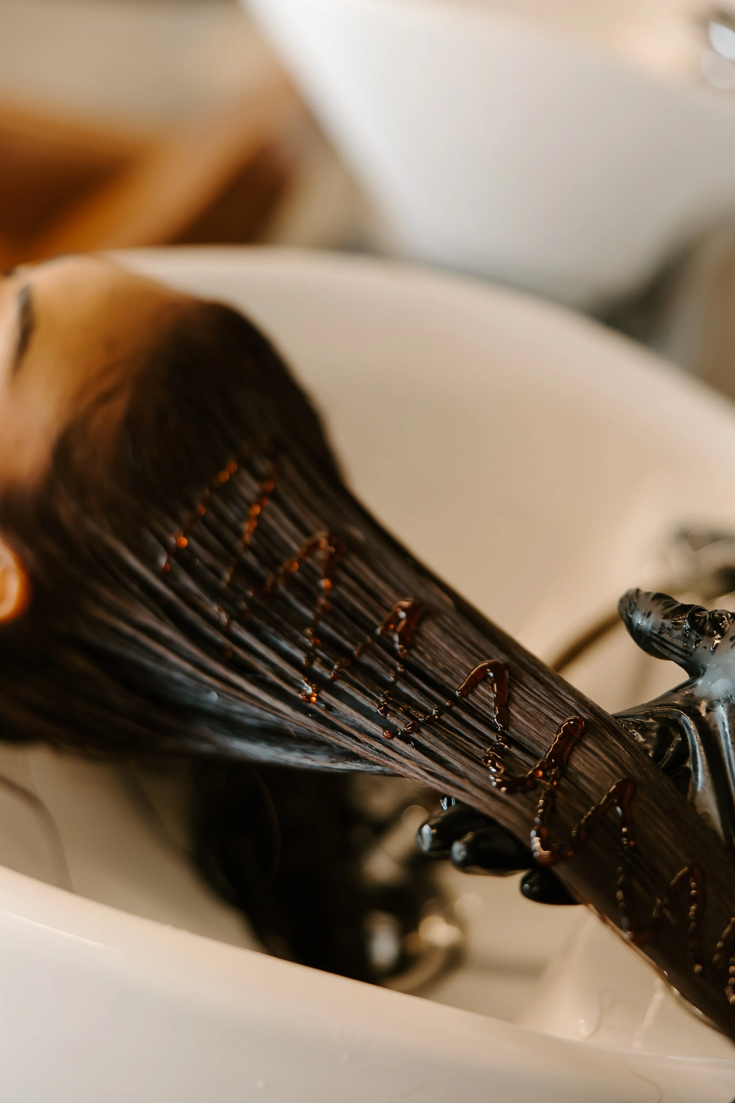 Close-up of a woman with dark hair styled straight, lying down with wet hair, and the word 'love' written in the hair with a dark substance.
