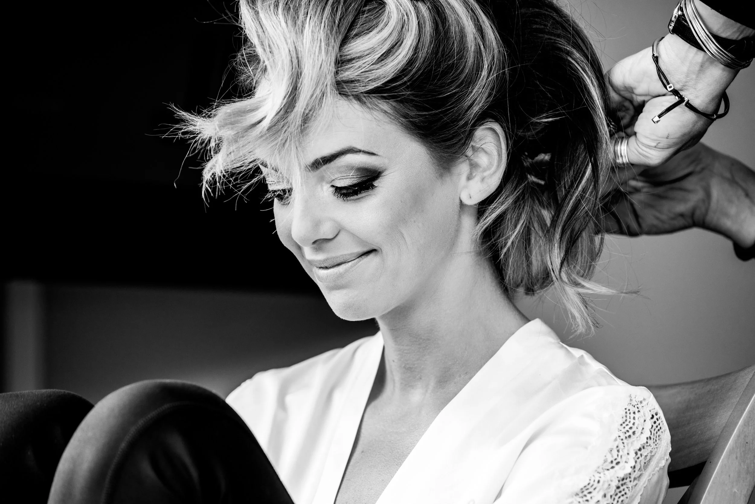 A woman with styled hair is getting her hair done by a hairstylist. The photo is in black and white.