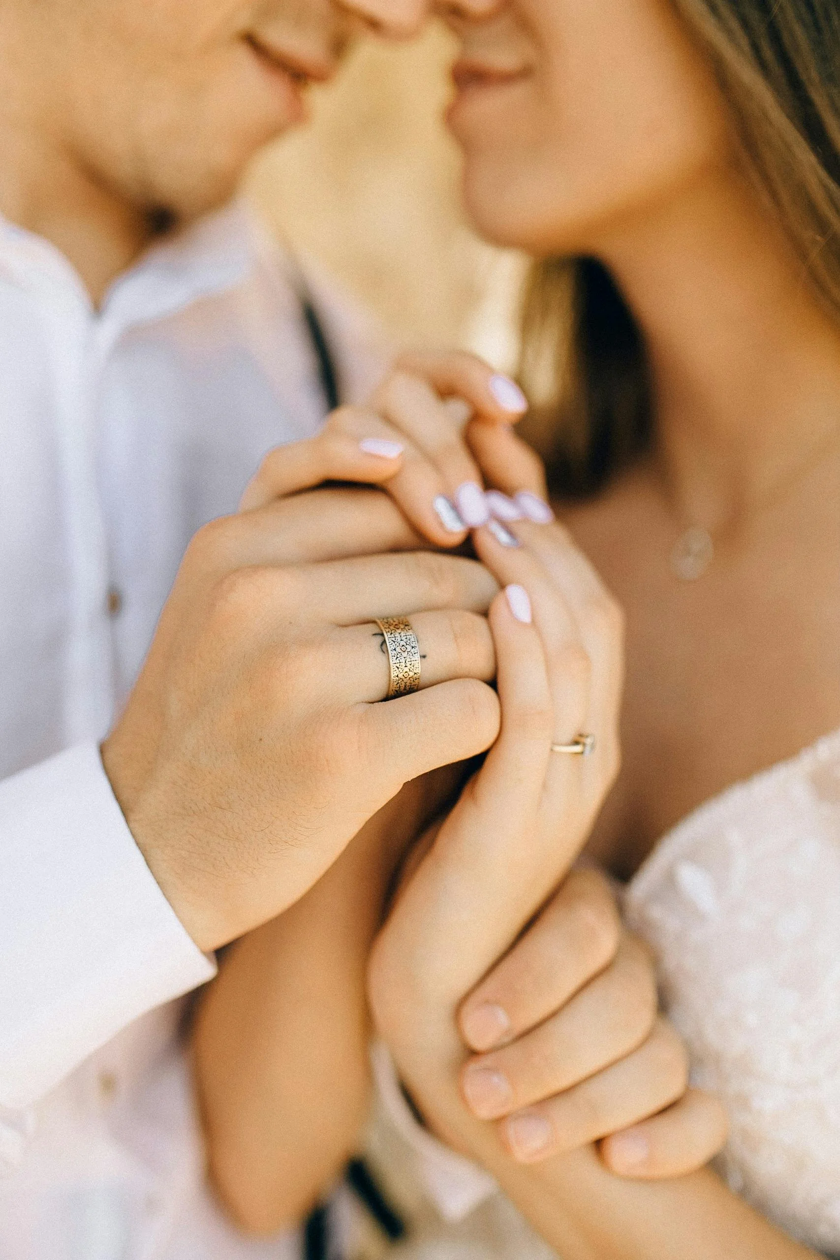 Close-up of a couple holding hands with wedding rings, touching their foreheads together.